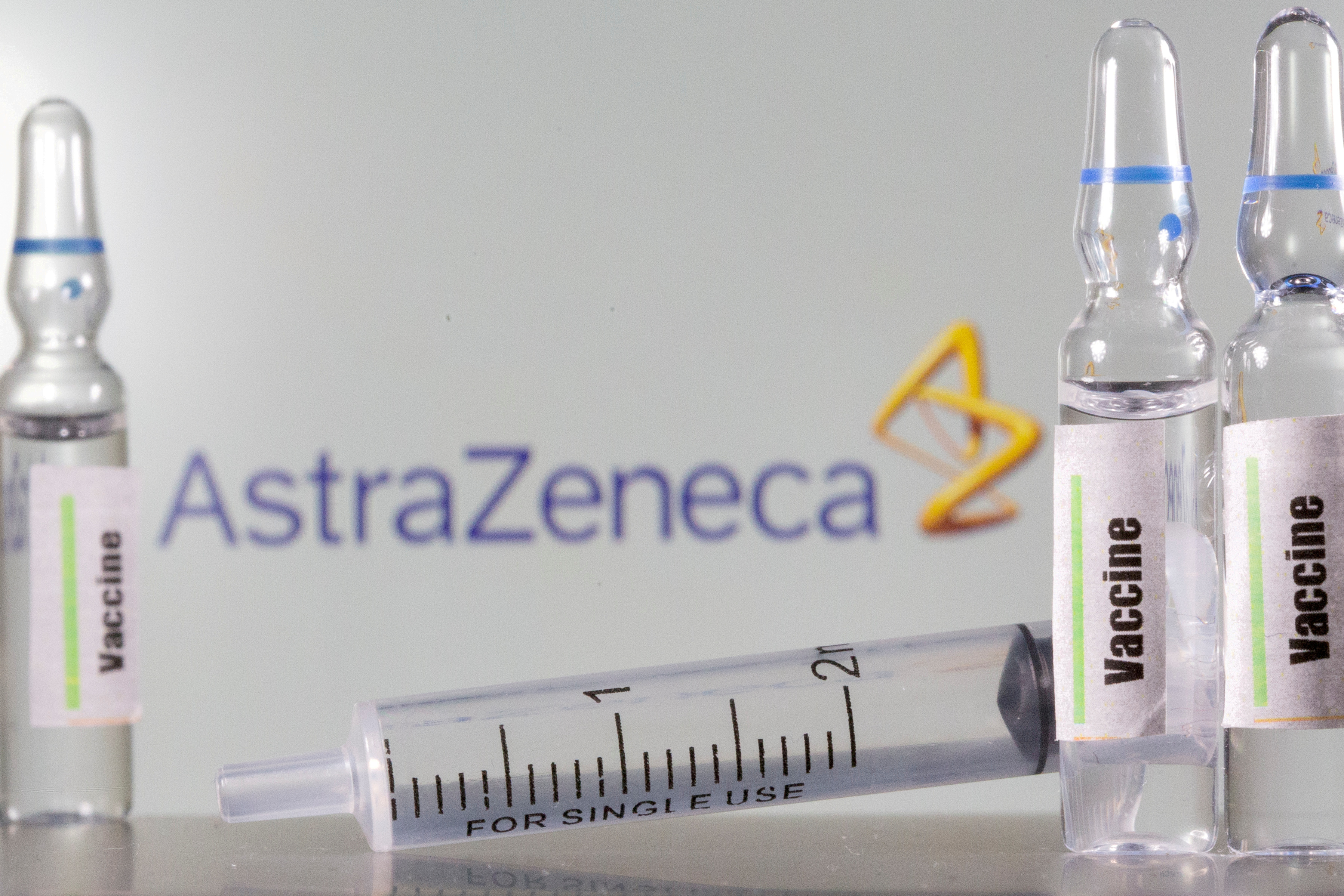 A test tube labelled 'vaccine' is seen in front of an AstraZeneca logo in this illustration
