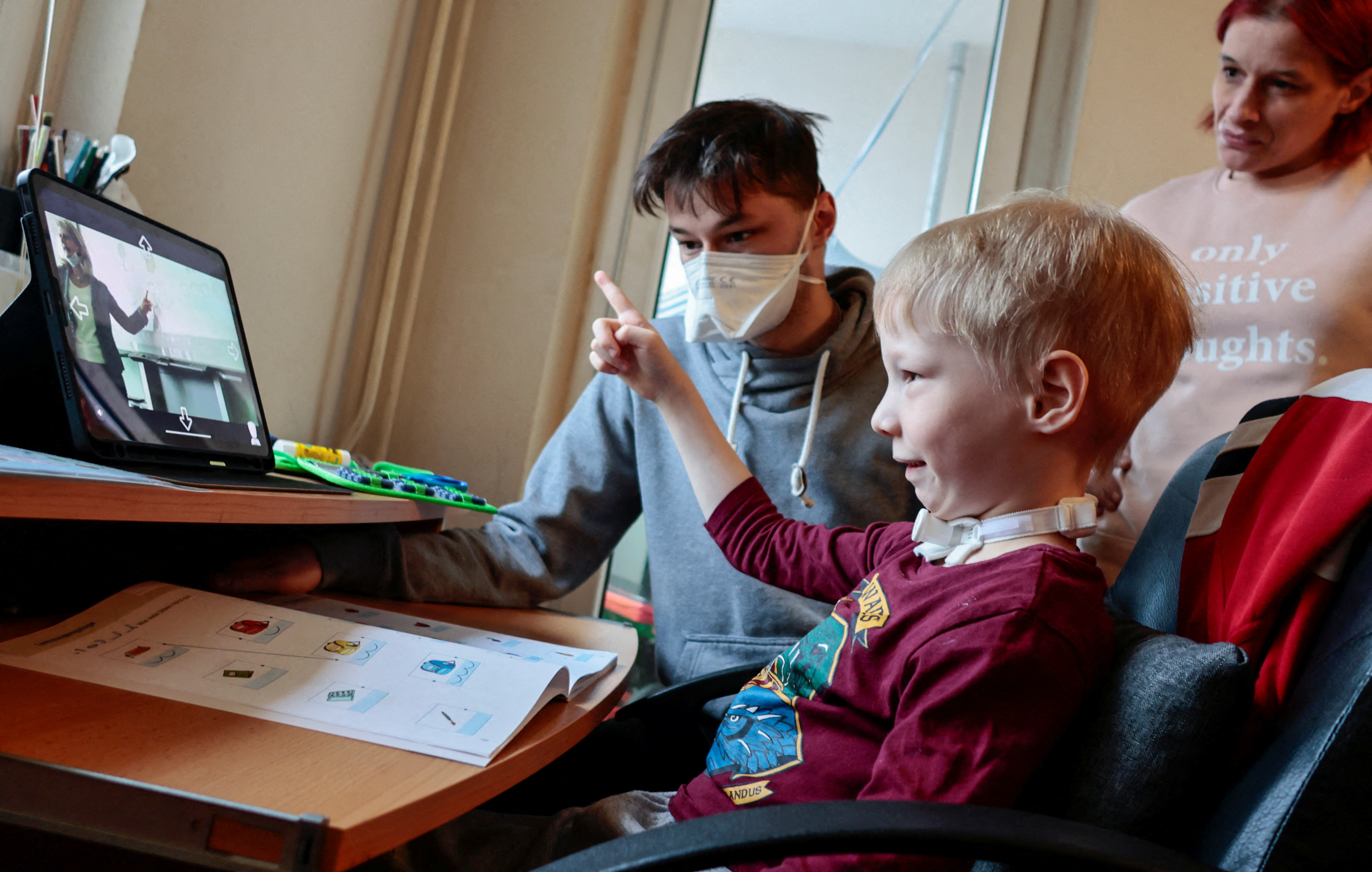 Седемгодишен ученик Джошуа посещава училищен урок, седнал до майка си Симоне и брат си Мартин, чрез робот-аватар в класната си стая, Берлин, Германия, 13 януари 2022 г. REUTERS/Hannibal Hanschke