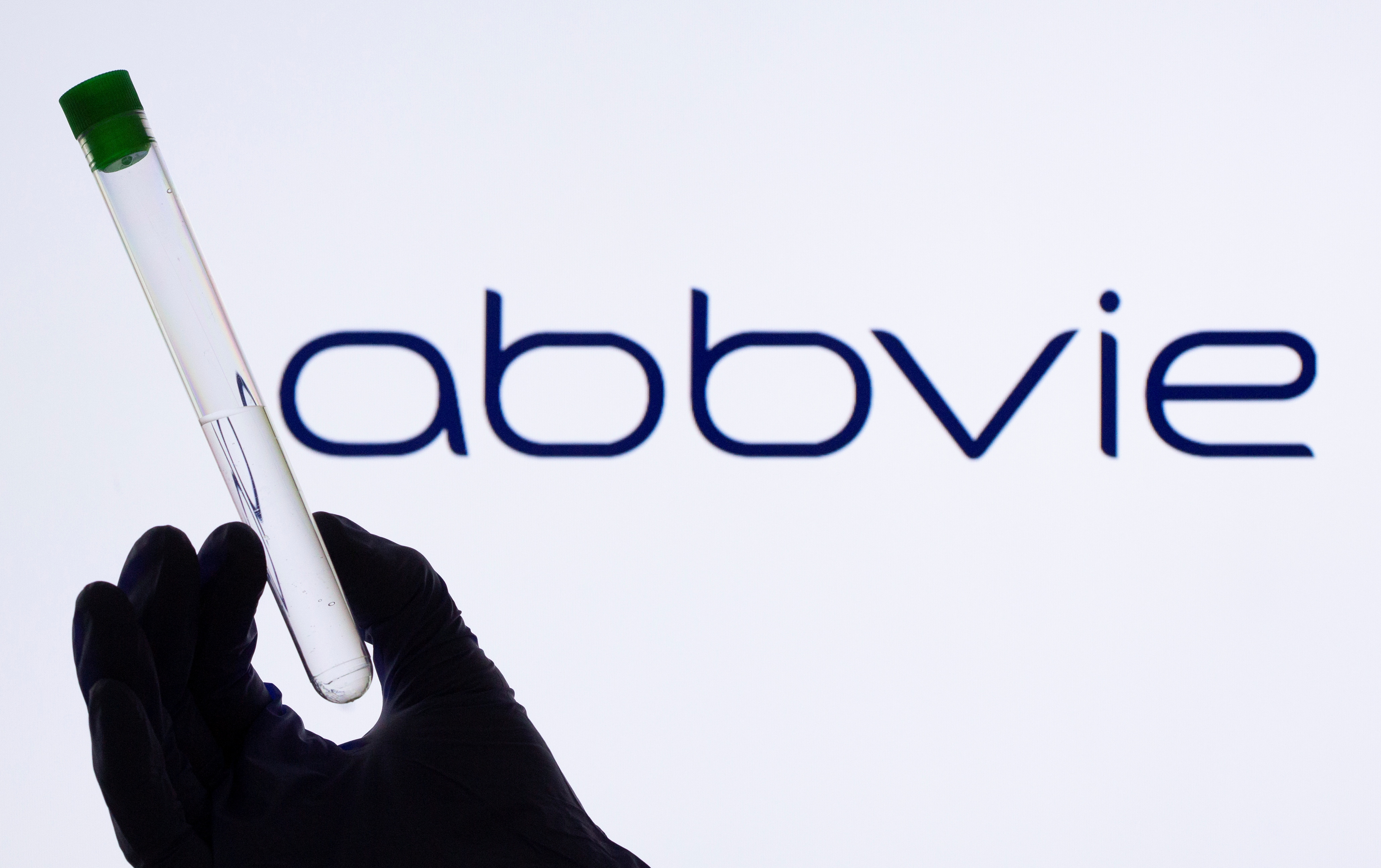 A woman holds a test tube in front of displayed Abbvie logo in this illustration
