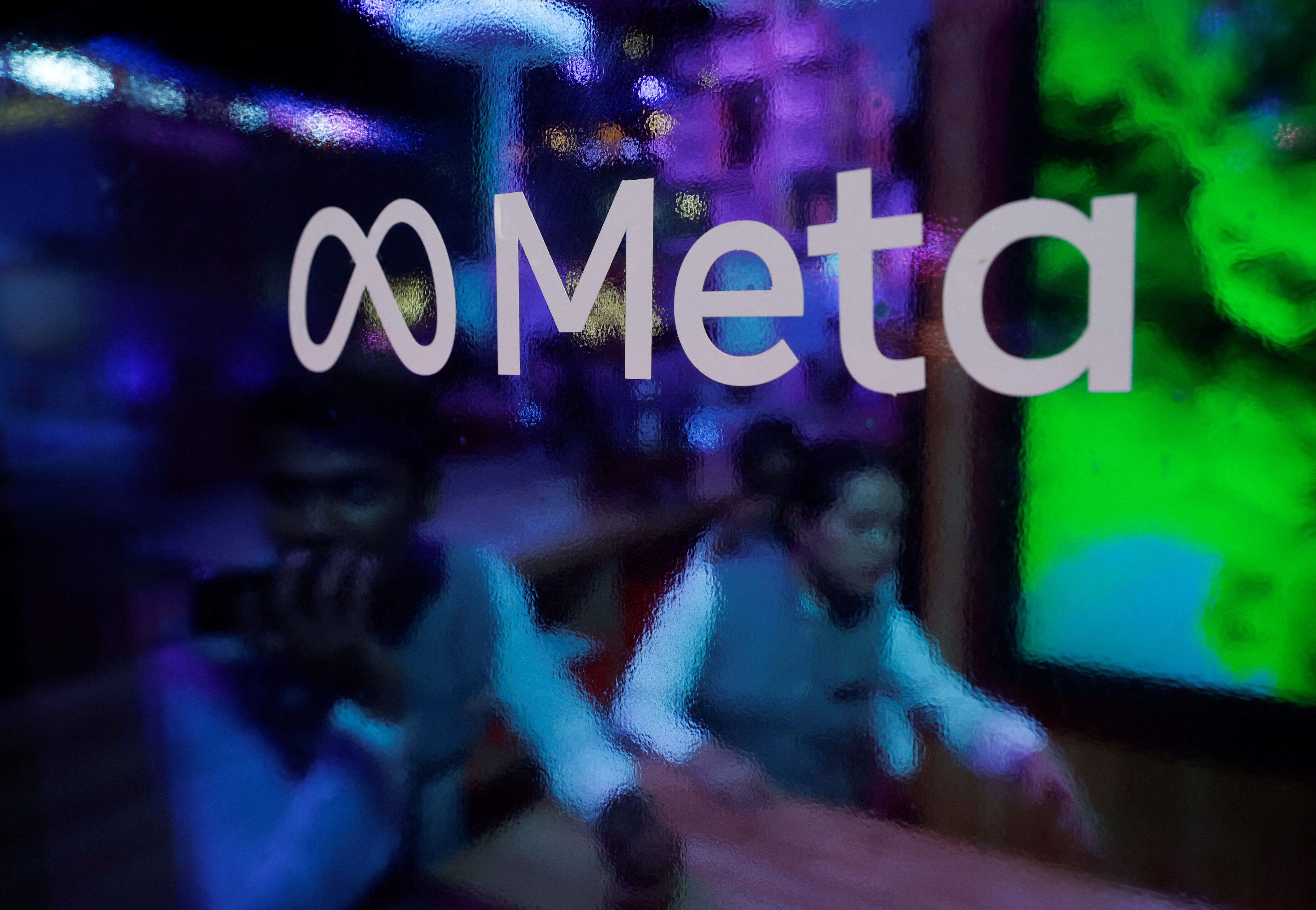 People are seen behind a logo of Meta Platforms, during a conference in Mumbai
