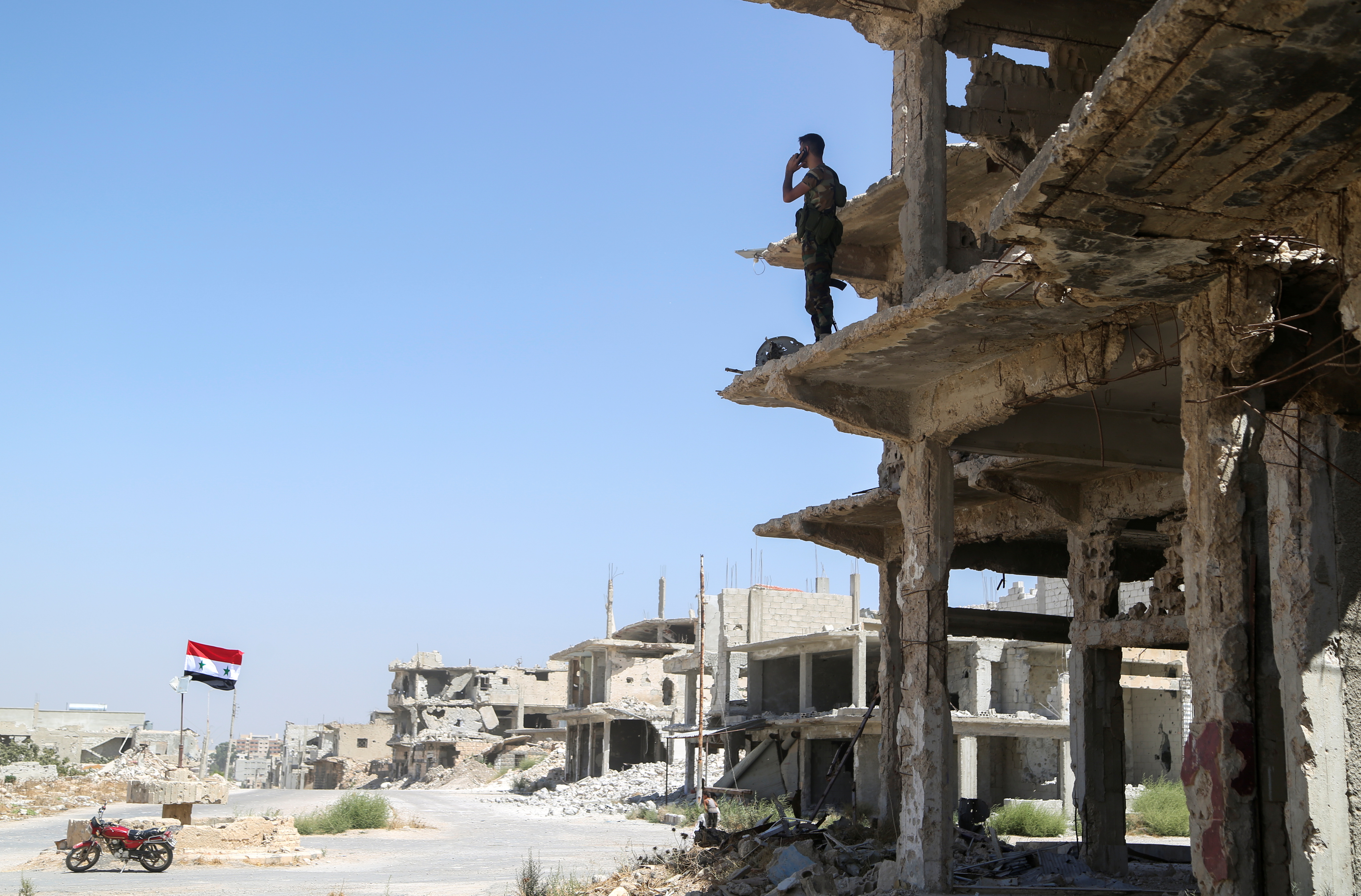 A Syrian army soldier stands on a damaged building in Deraa al Balaad