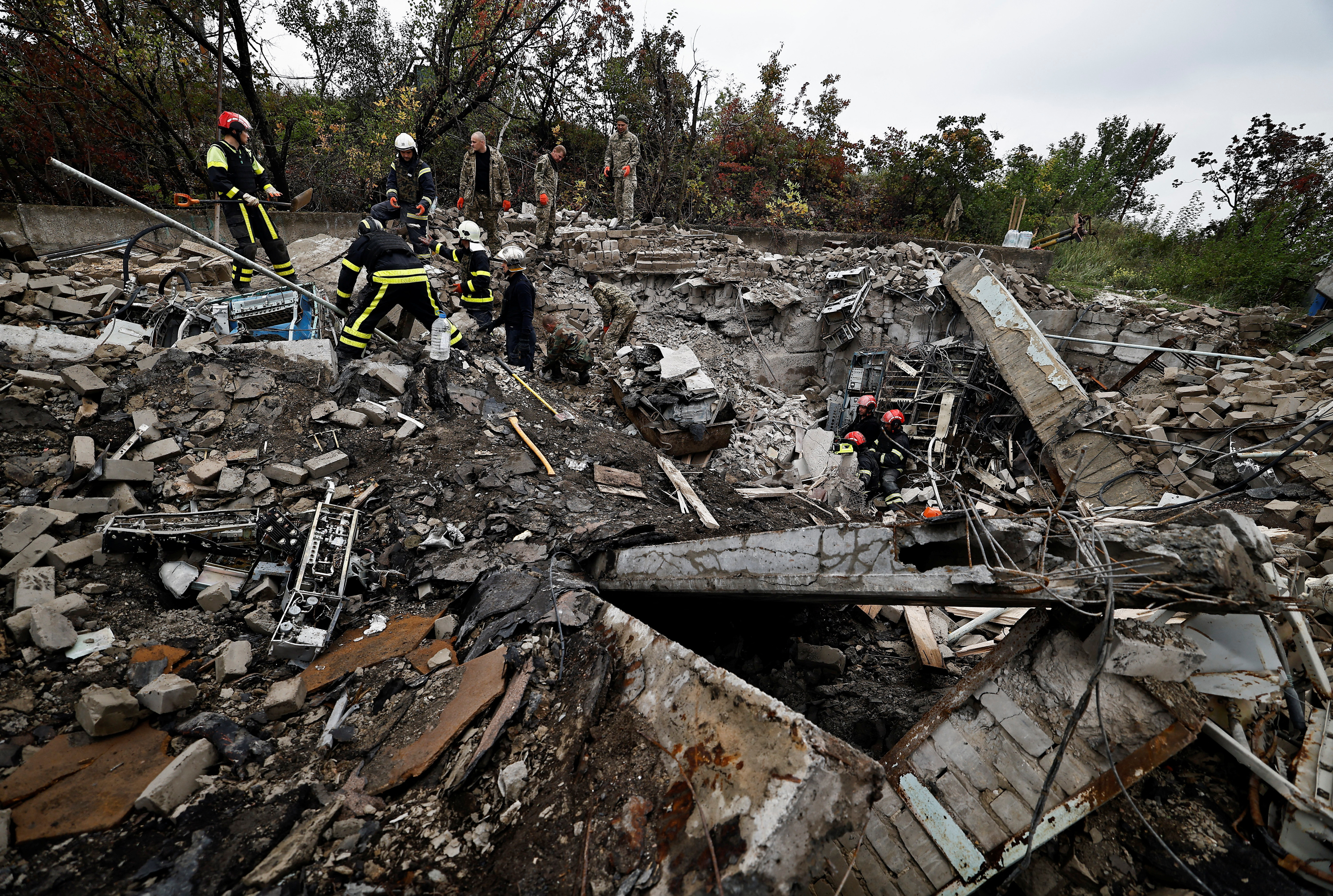Firefighters and Ukrainian army soldiers search for bodies of people killed during a Russian attack, among the remains of a building beside a TV tower, in the recently liberated town of Izium