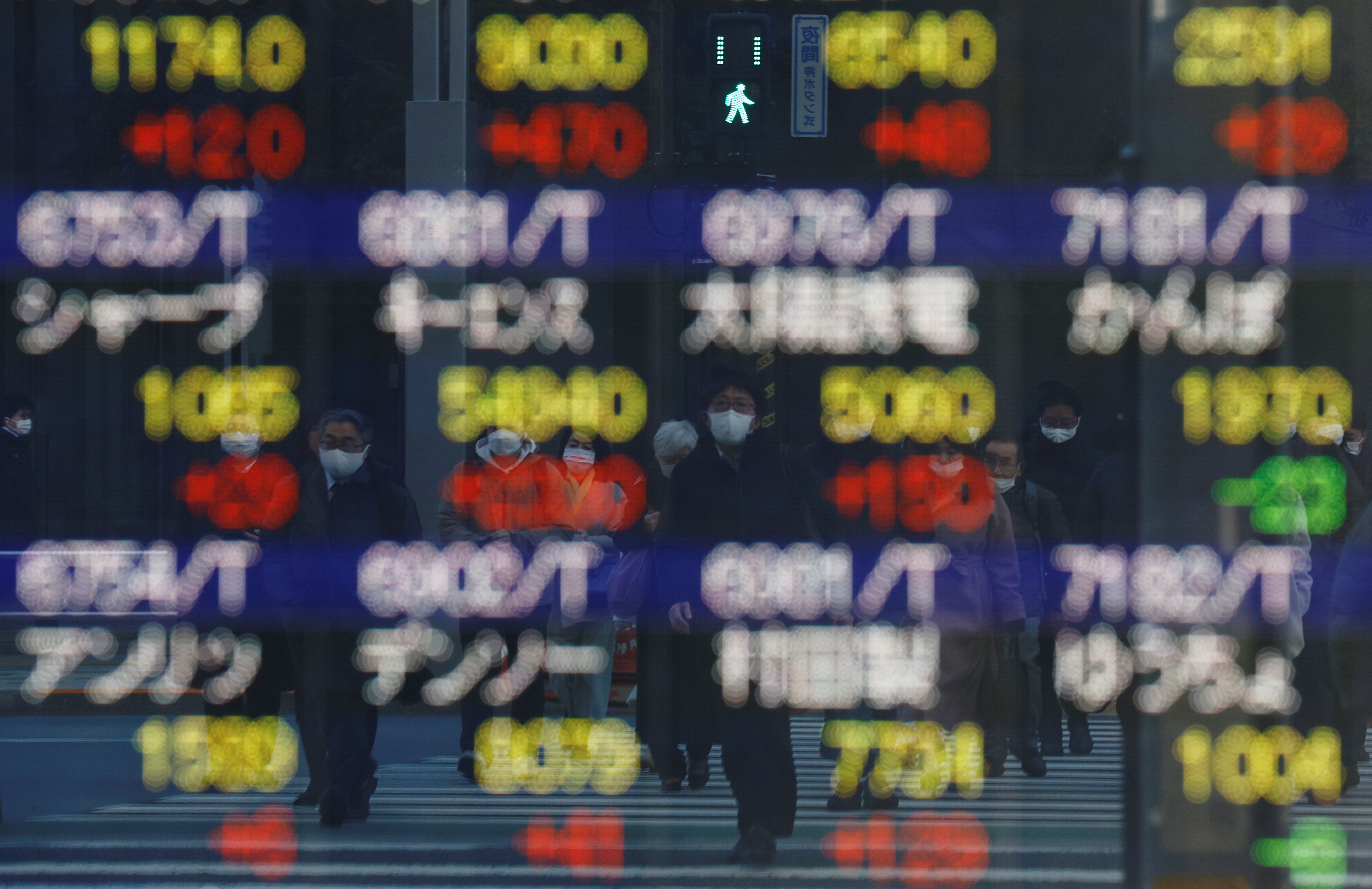 FILE PHOTO - Pedestrians wearing protective masks, amid the coronavirus disease (COVID-19) outbreak, are reflected on an electronic board outside a brokerage in Tokyo
