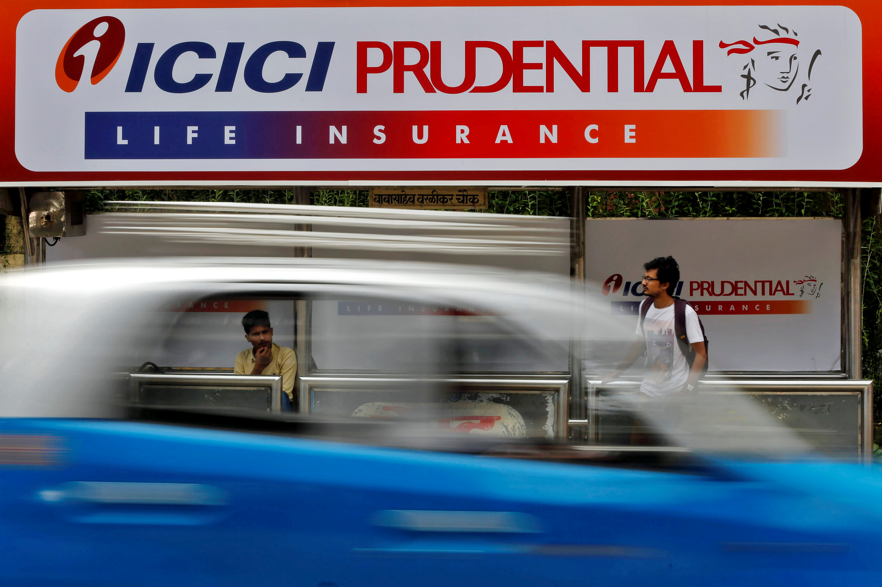 Passengers wait in front of an ICICI Prudential billboard at a bus stop in Mumbai