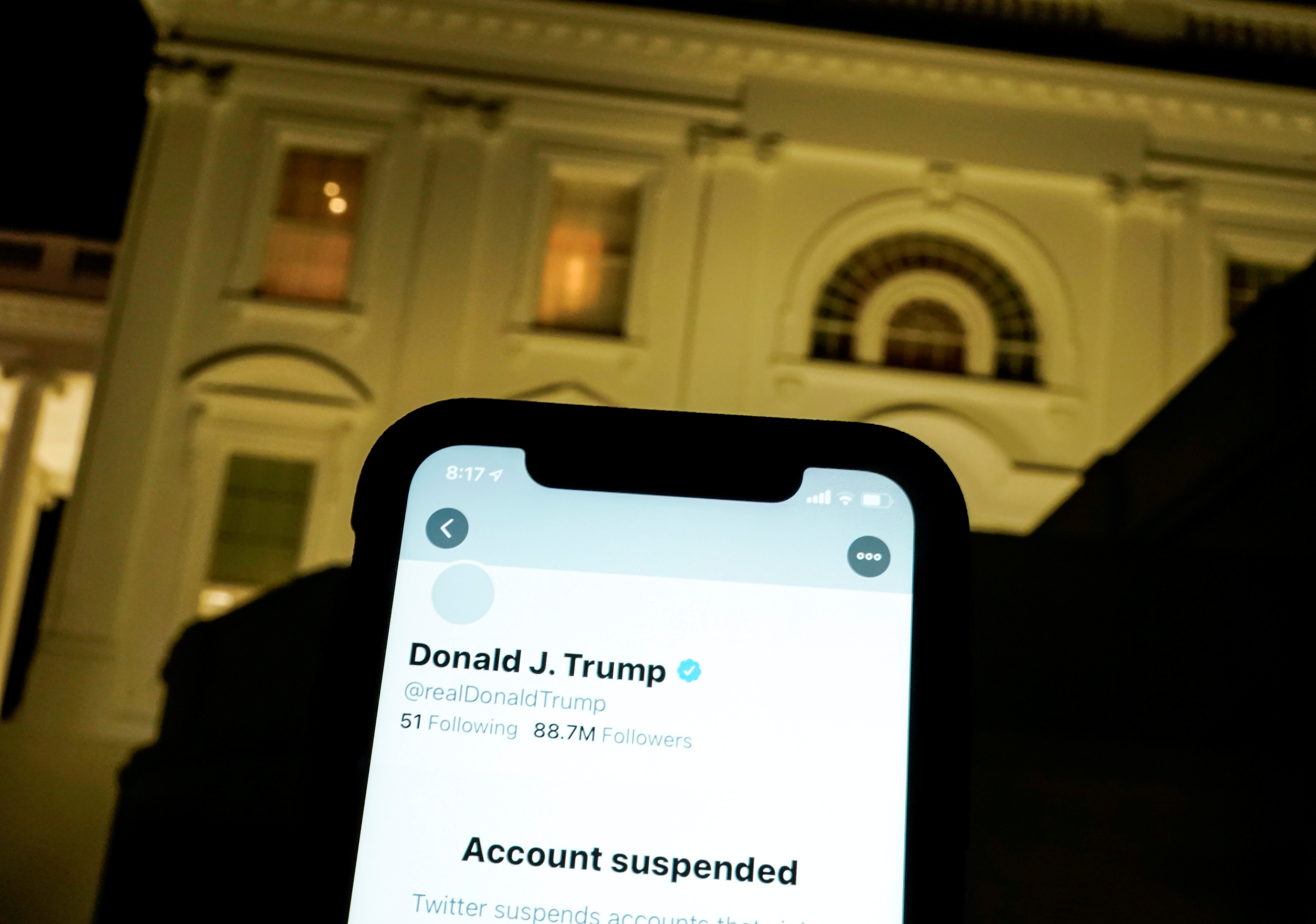 A photo illustration shows the suspended Twitter account of U.S. President Donald Trump on a smartphone and the White House in Washington