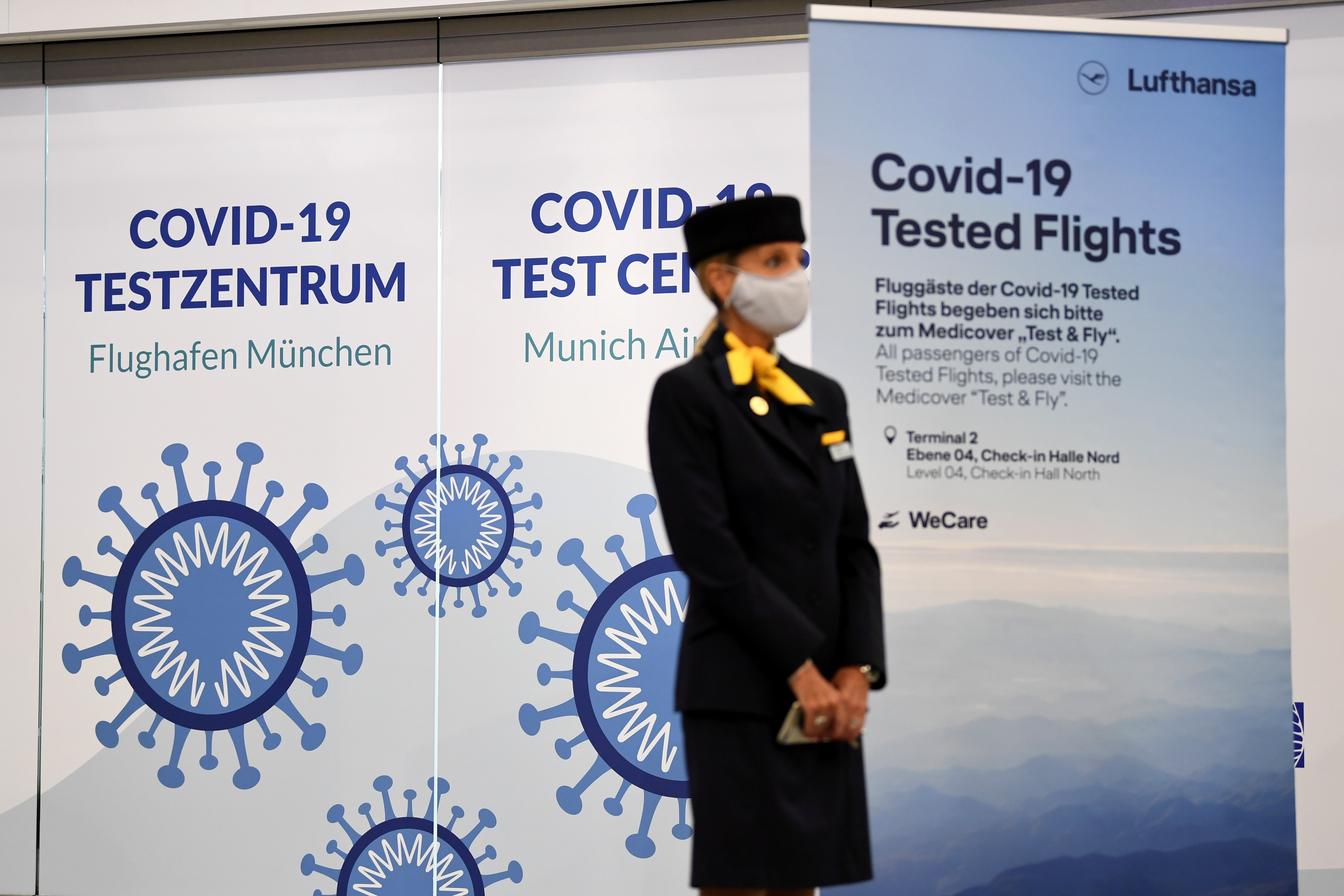 Lufthansa employee stands in front of a poster at new COVID-19 quick test center at Franz-Josef-Strauss airport in Munich
