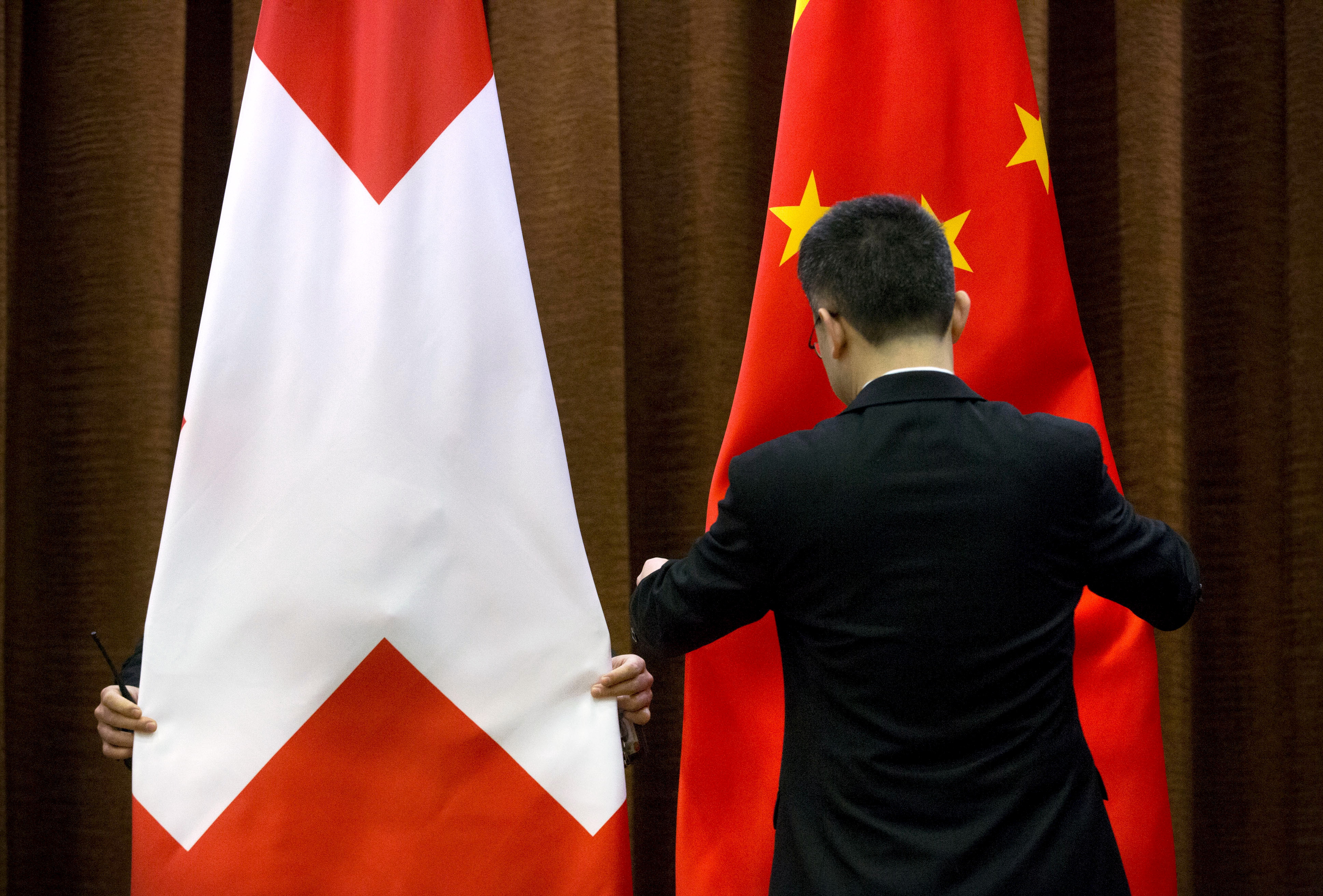 Workers adjust a Swiss and Chinese flag before a bilateral meeting between Chinese Foreign Minister Wang Yi and Swiss Foreign Minister Didier Burkhalter at the Ministry of Foreign Affairs in Beijing