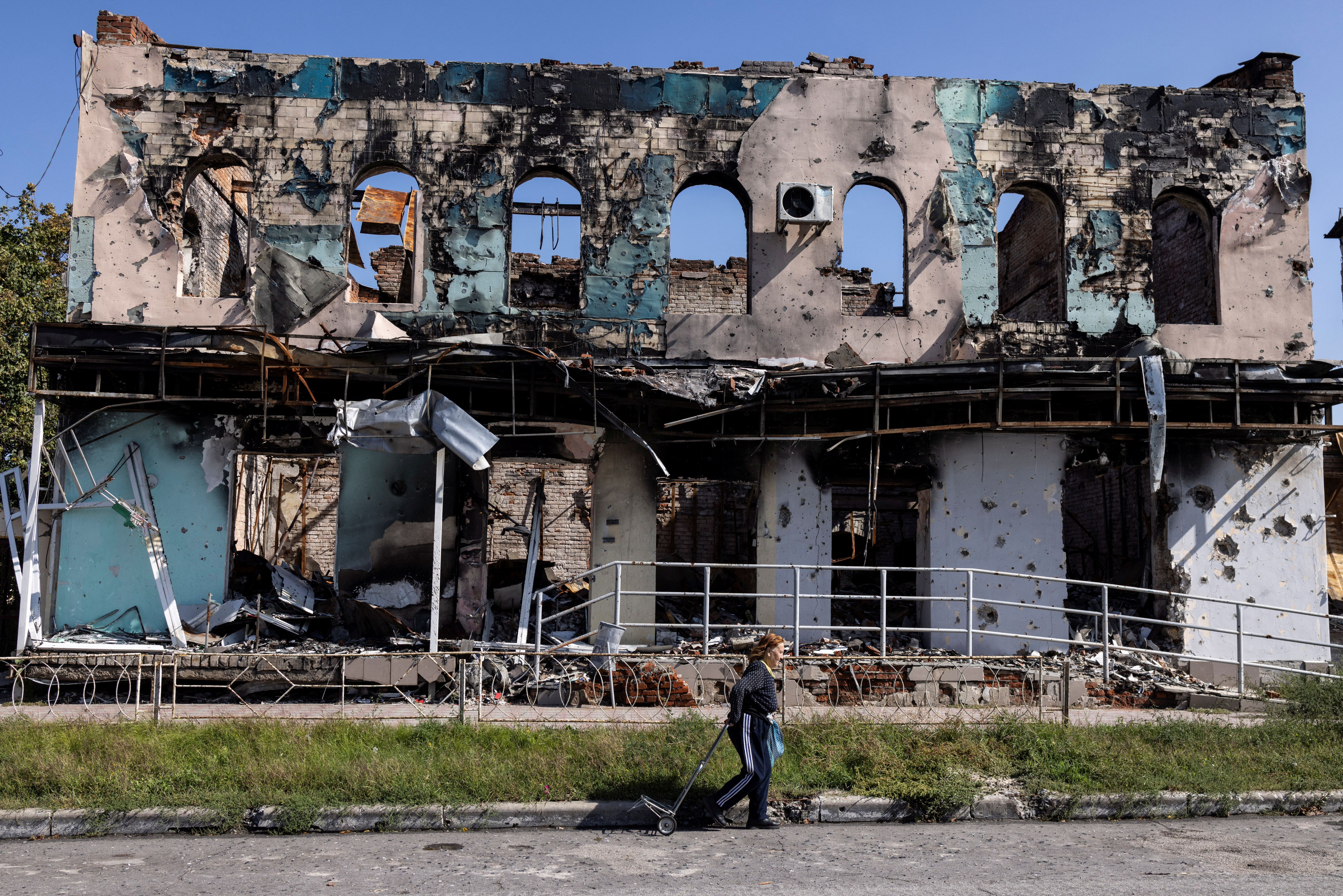 A woman walks past a destroyed building in Izium