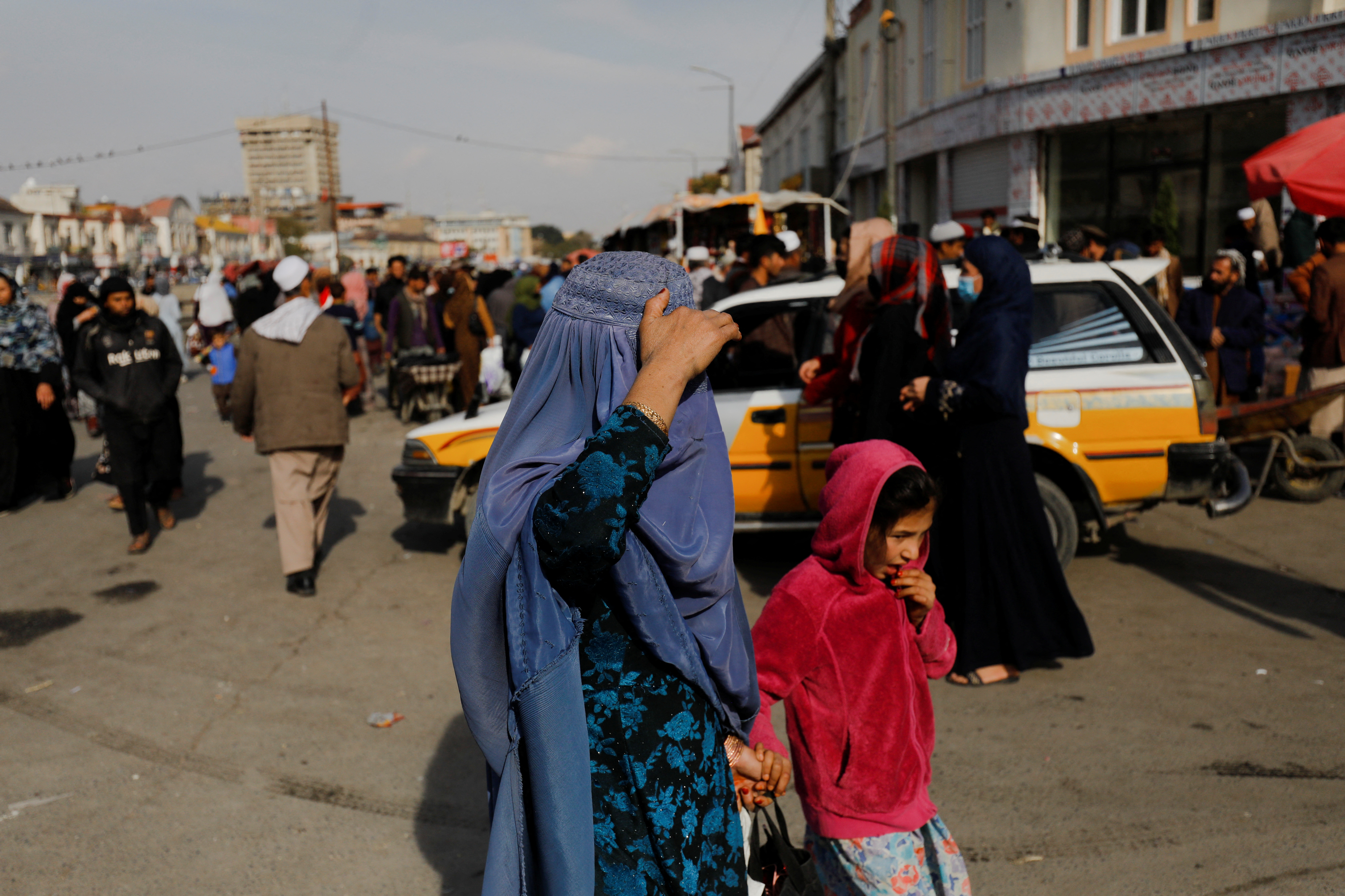 An Afghan woman and a girl walk in a street in Kabul