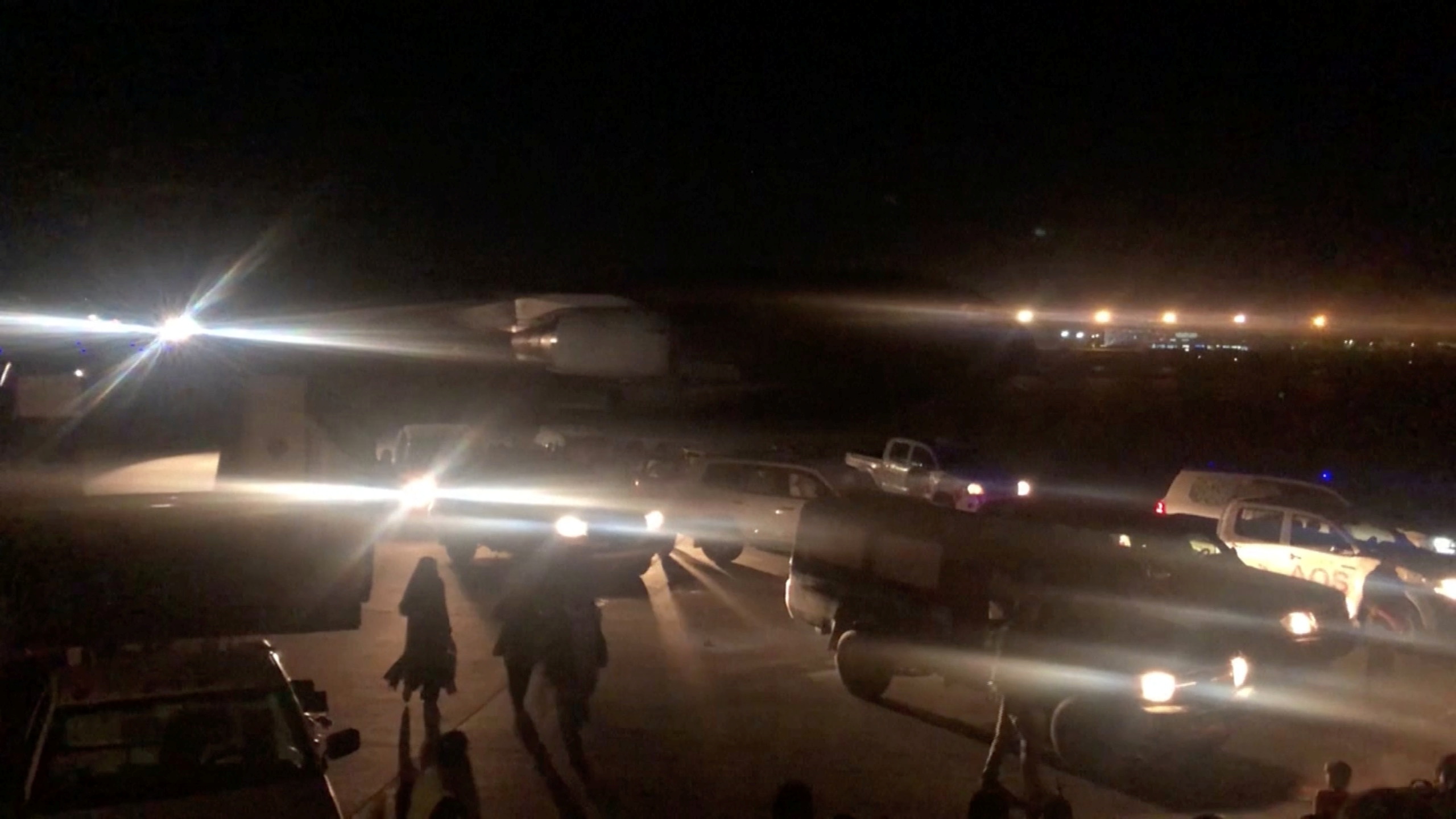 People walk past vehicles on the tarmac towards a plane at the airport in Kabul