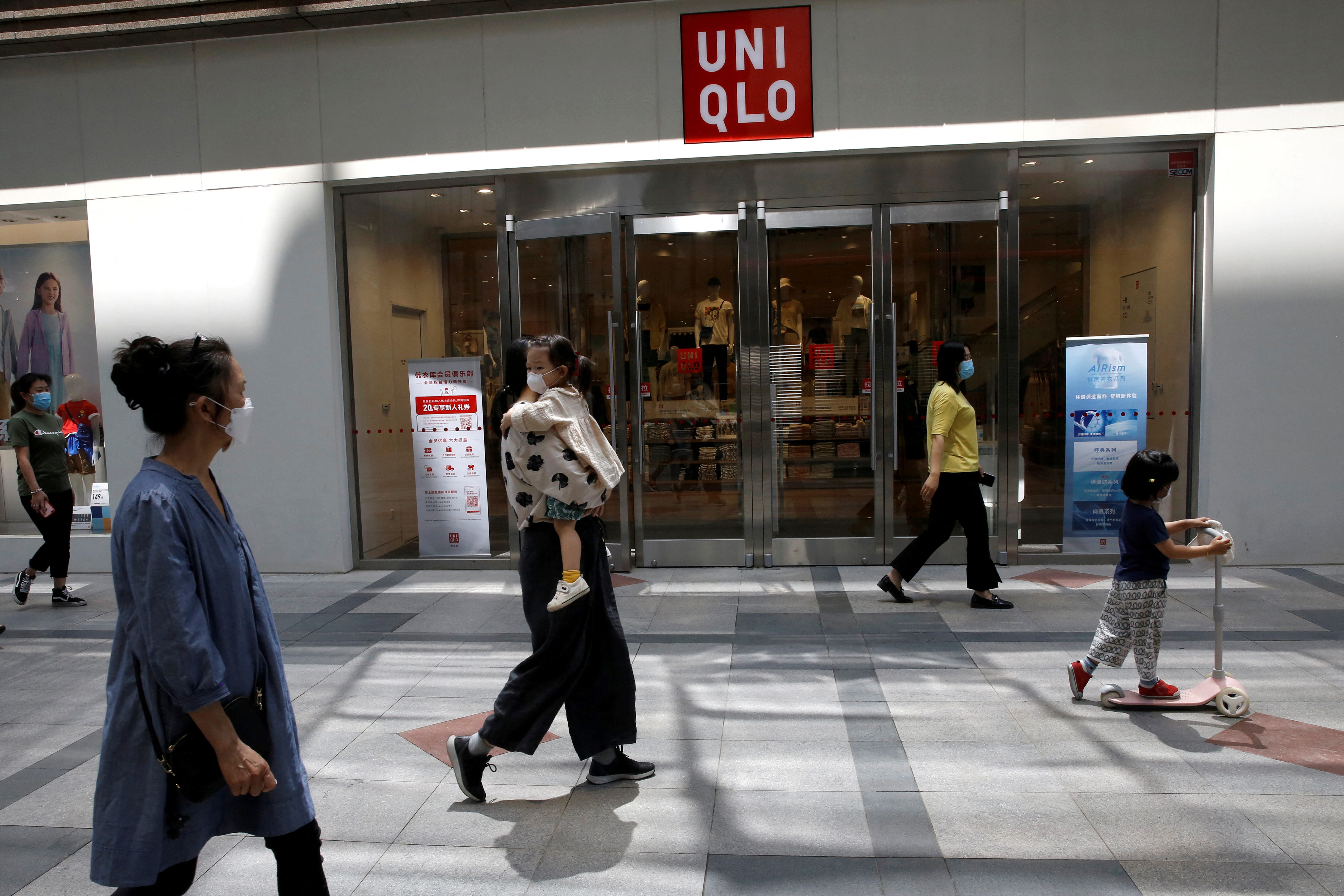 People wearing face masks walk past a store of Fast Retailing's fashion chain Uniqlo in Beijing