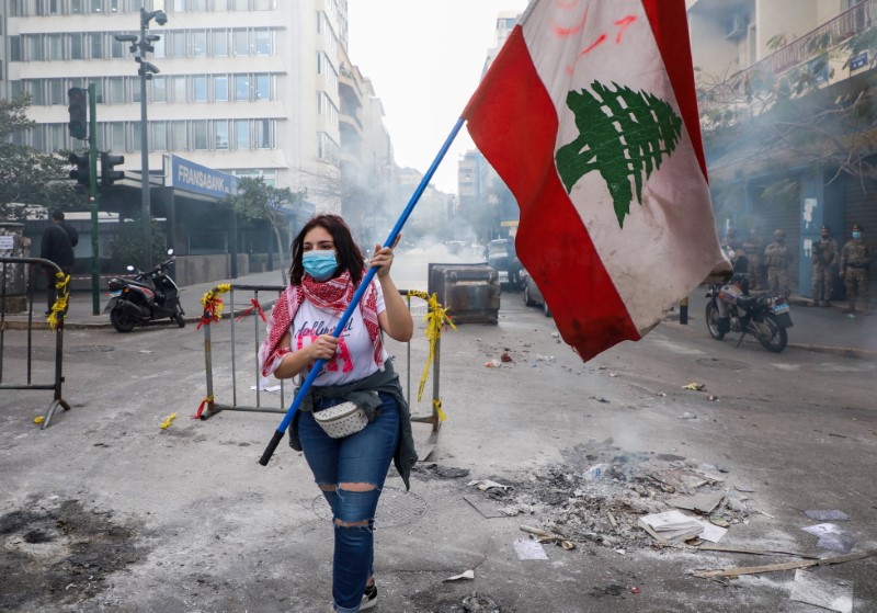 A demonstrator carries a national flag along a blocked road, during a protest against the fall in Lebanese pound currency and mounting economic hardships, near the Central Bank building, in Beirut, Lebanon March 16, 2021. REUTERS/Mohamed Azakir/File Photo
