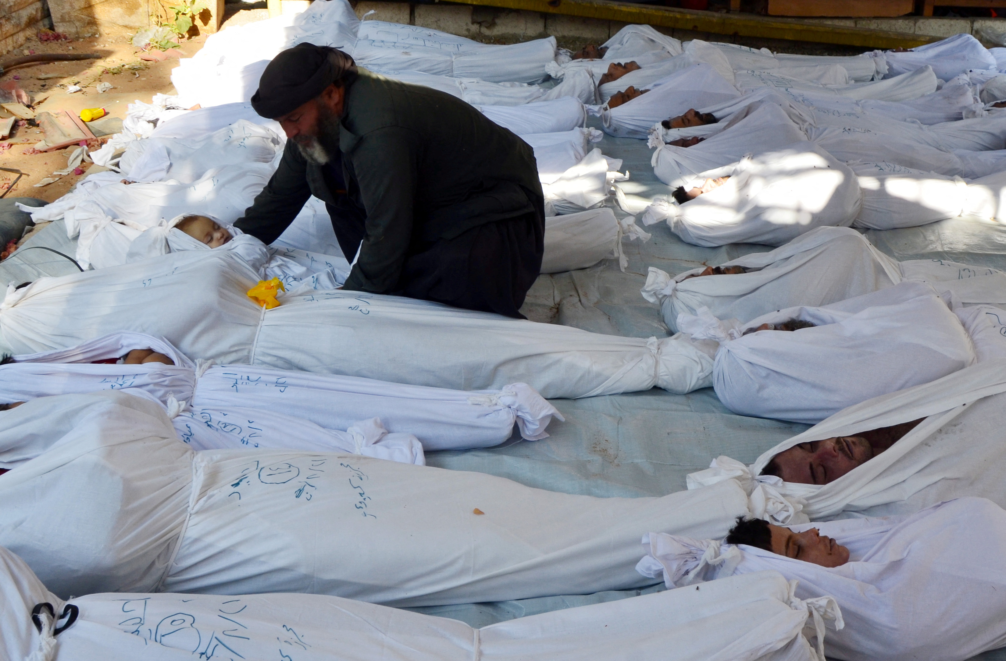 A man holds the body of a dead child among bodies of people in the Douma neighbourhood of Damascus