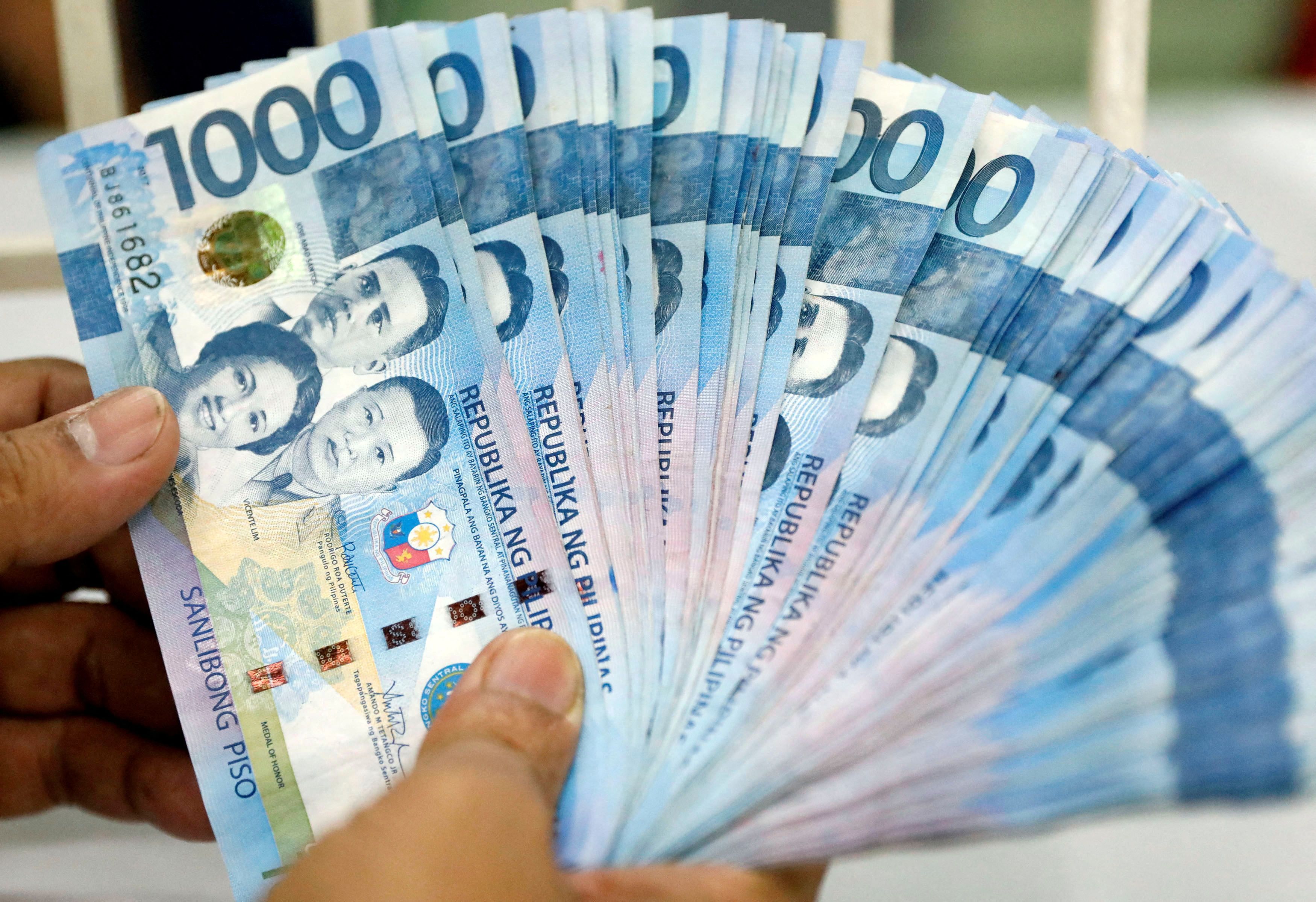 A worker shows Philippine peso bills inside a money changer in metro Manila