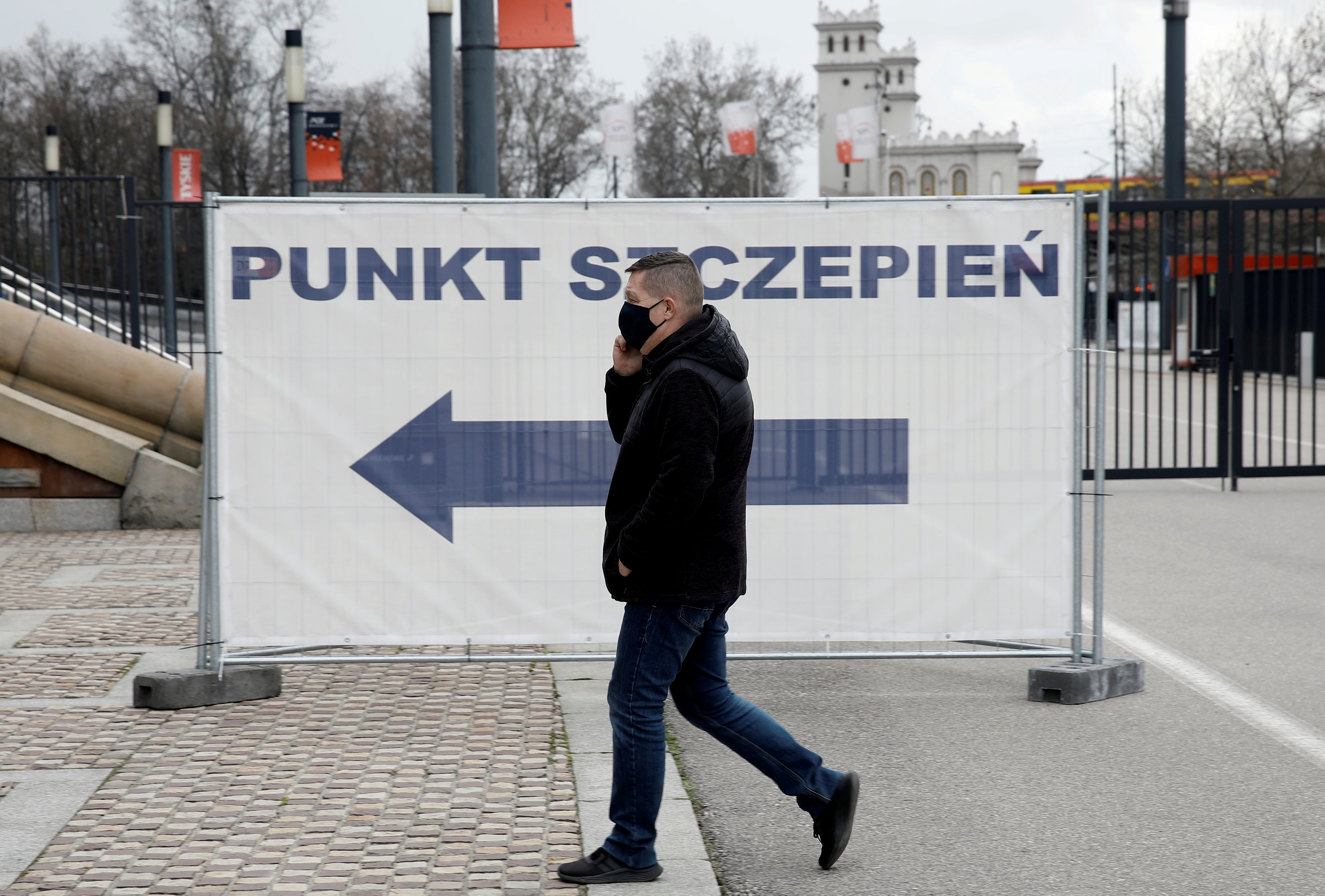 A man wearing a protective mask walks near the coronavirus vaccine centre located in a temporary hospital organised at National Stadium in Warsaw, Poland