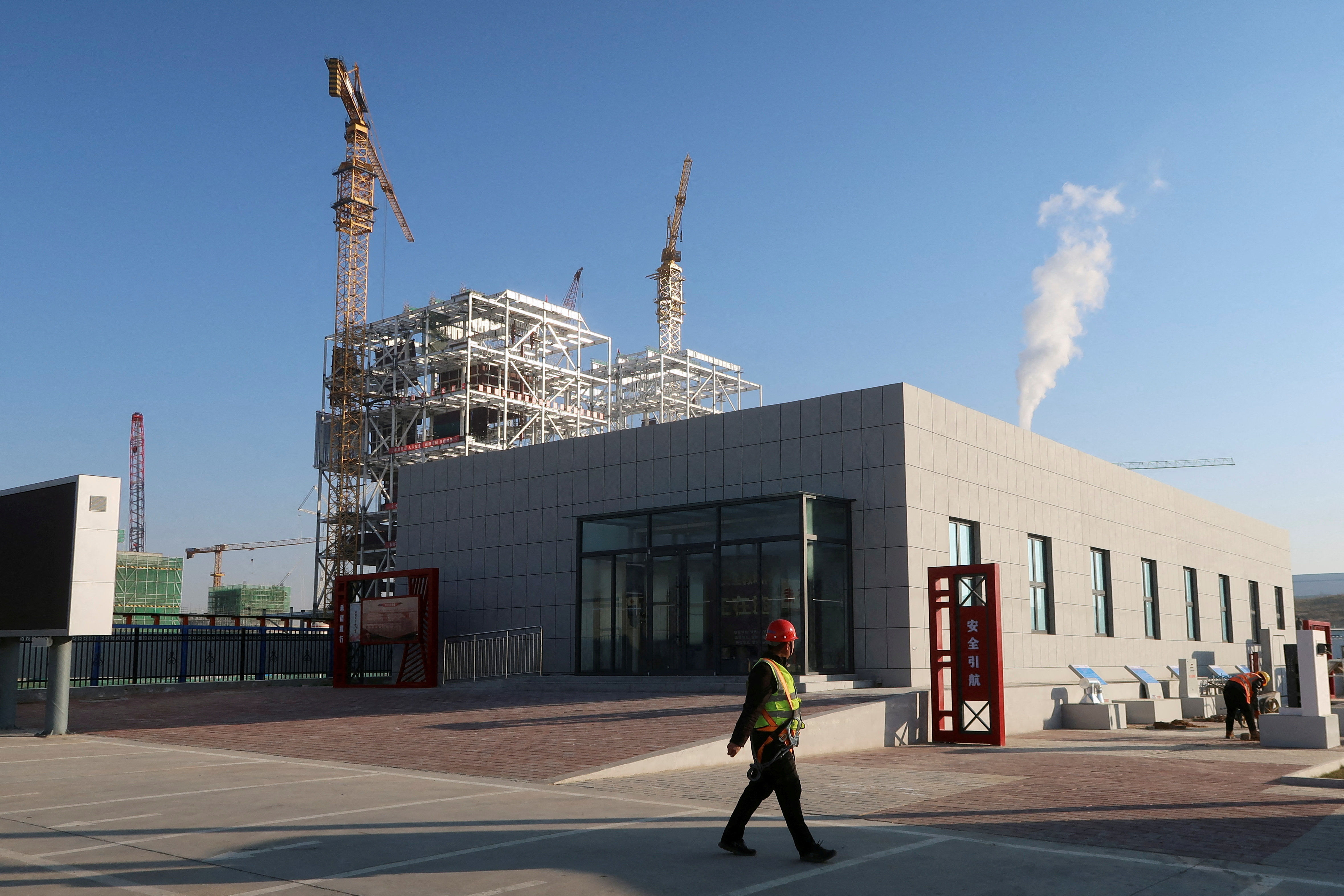 Worker walks past cranes at Yushen Yuheng power plant, a coal-fired power plant under construction, in Yulin