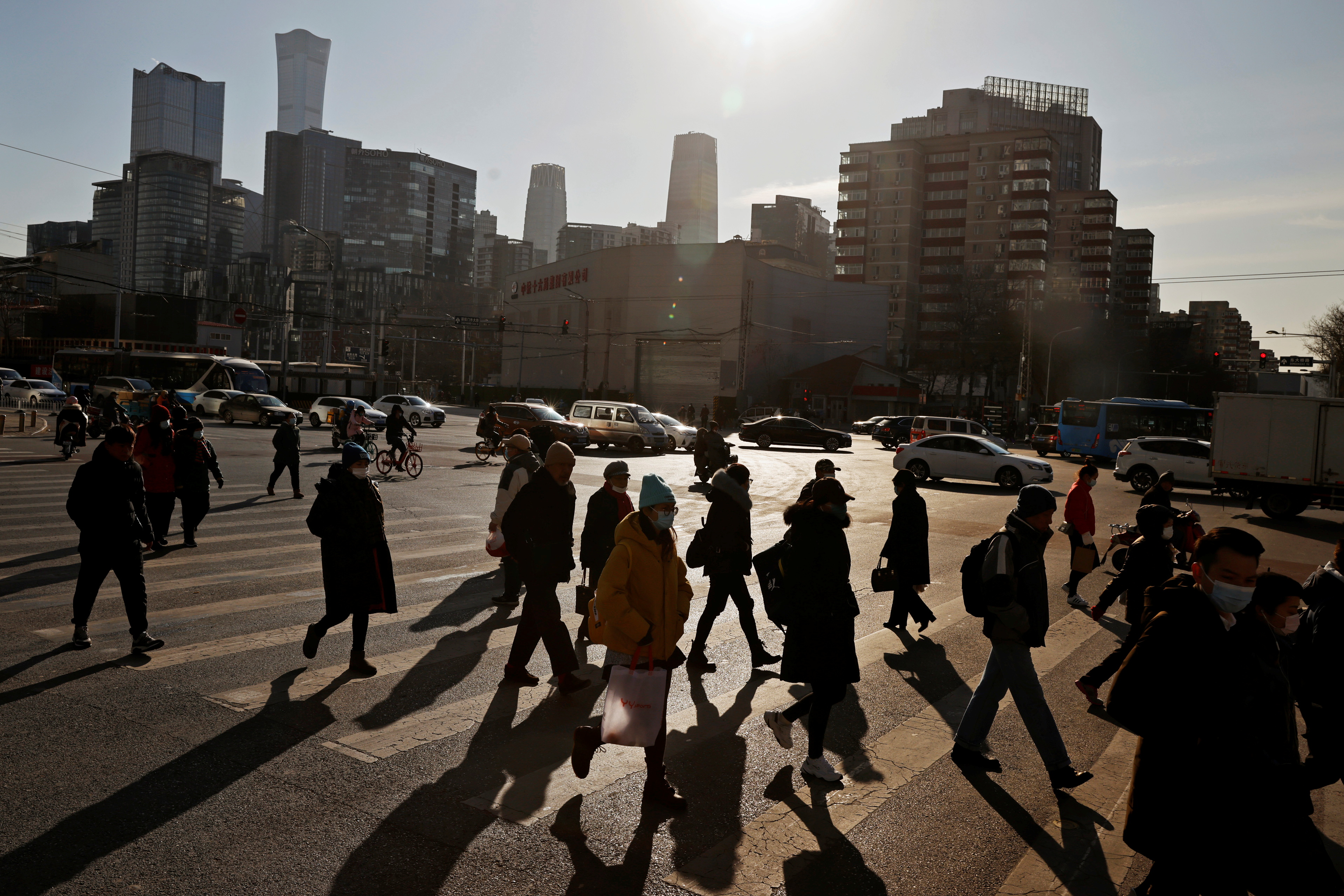People cross a street during morning rush hour in front of the skyline of the CBD in Beijing