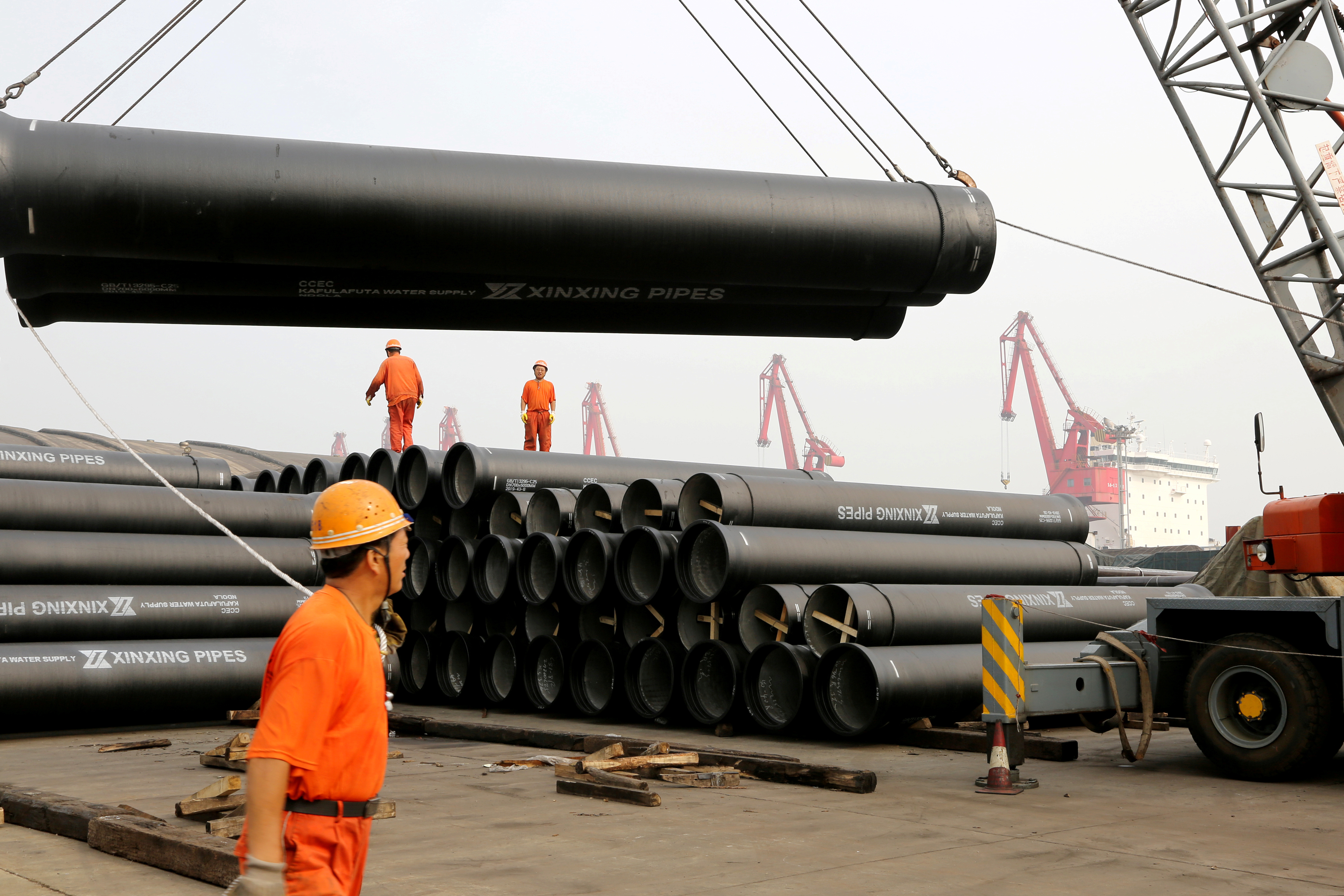 Workers direct a crane lifting ductile iron pipes for export at a port in Lianyungang, Jiangsu