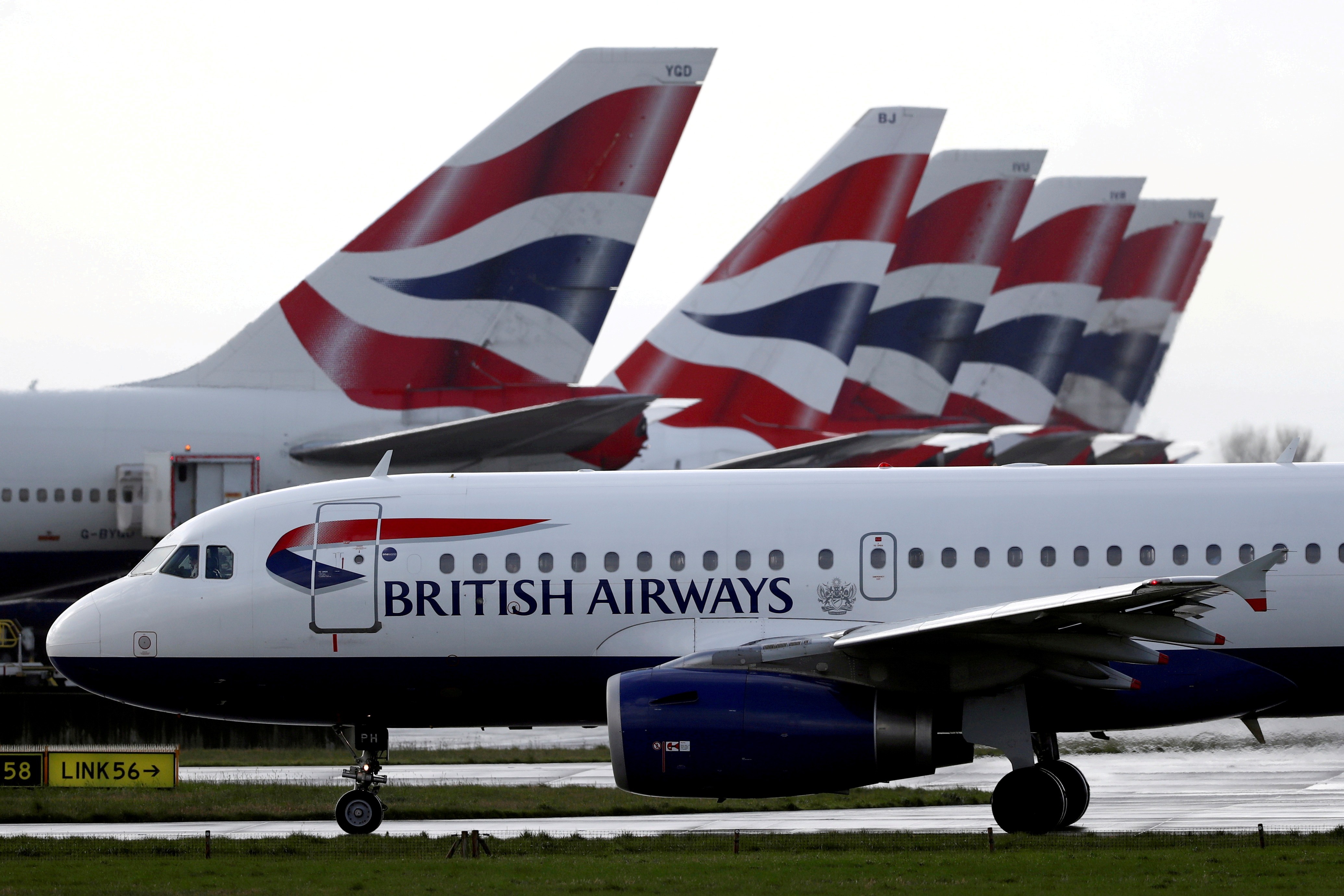 A British Airways plane taxis past tail fins of parked aircraft at Heathrow Airport in London