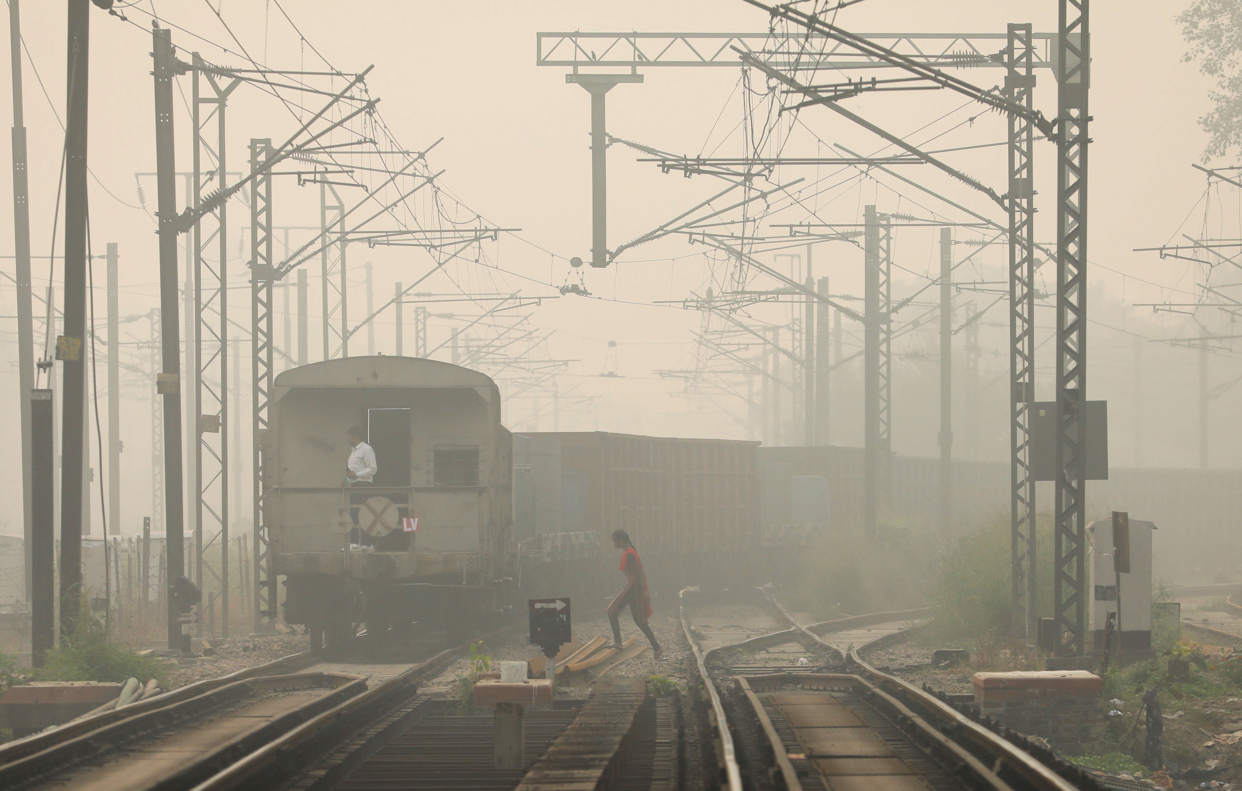 A woman crosses railway tracks as a goods train passes by, on a smoggy day in New Delhi