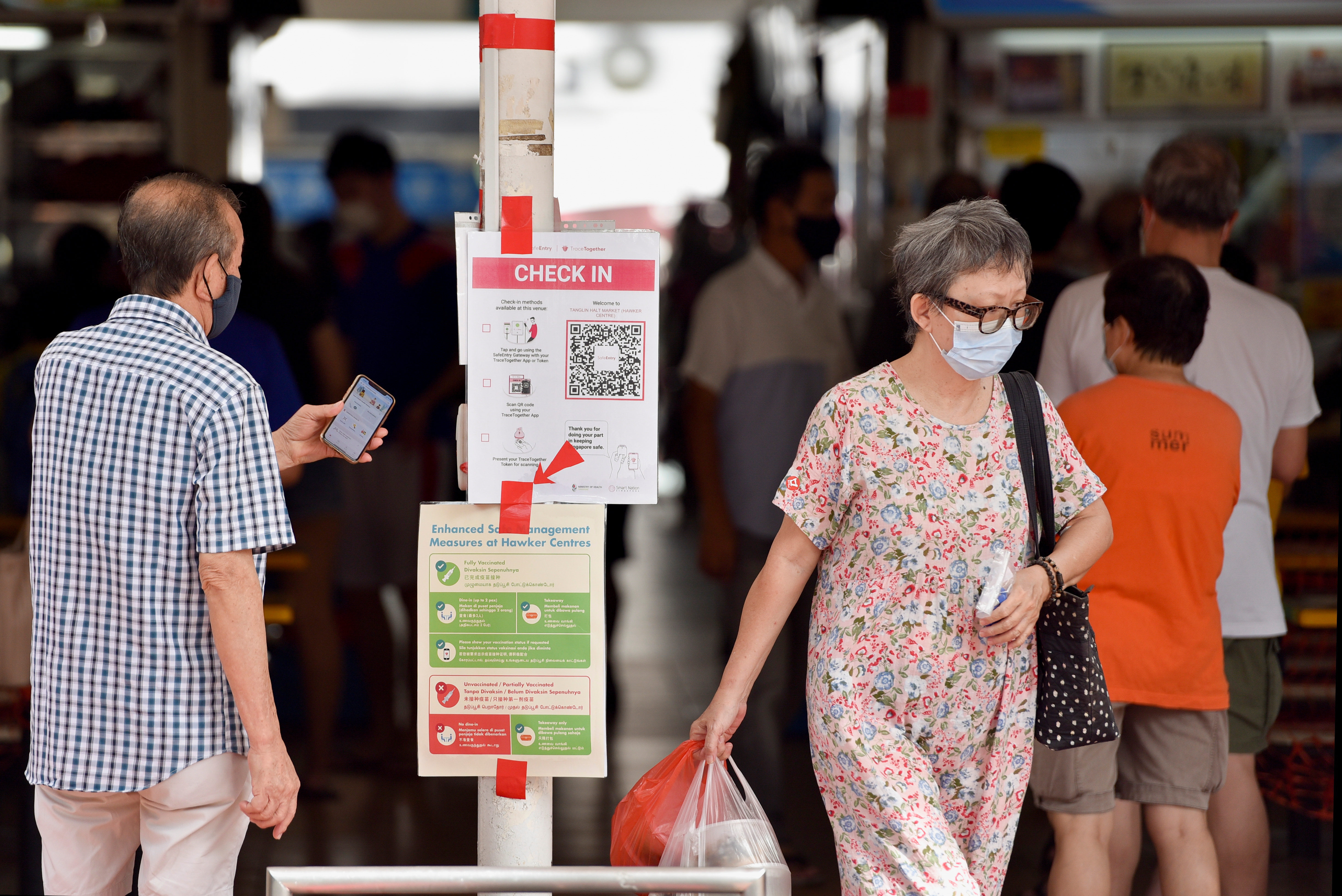 People entering a food centre check-in with their phones before they are allowed to dine-in in Singapore