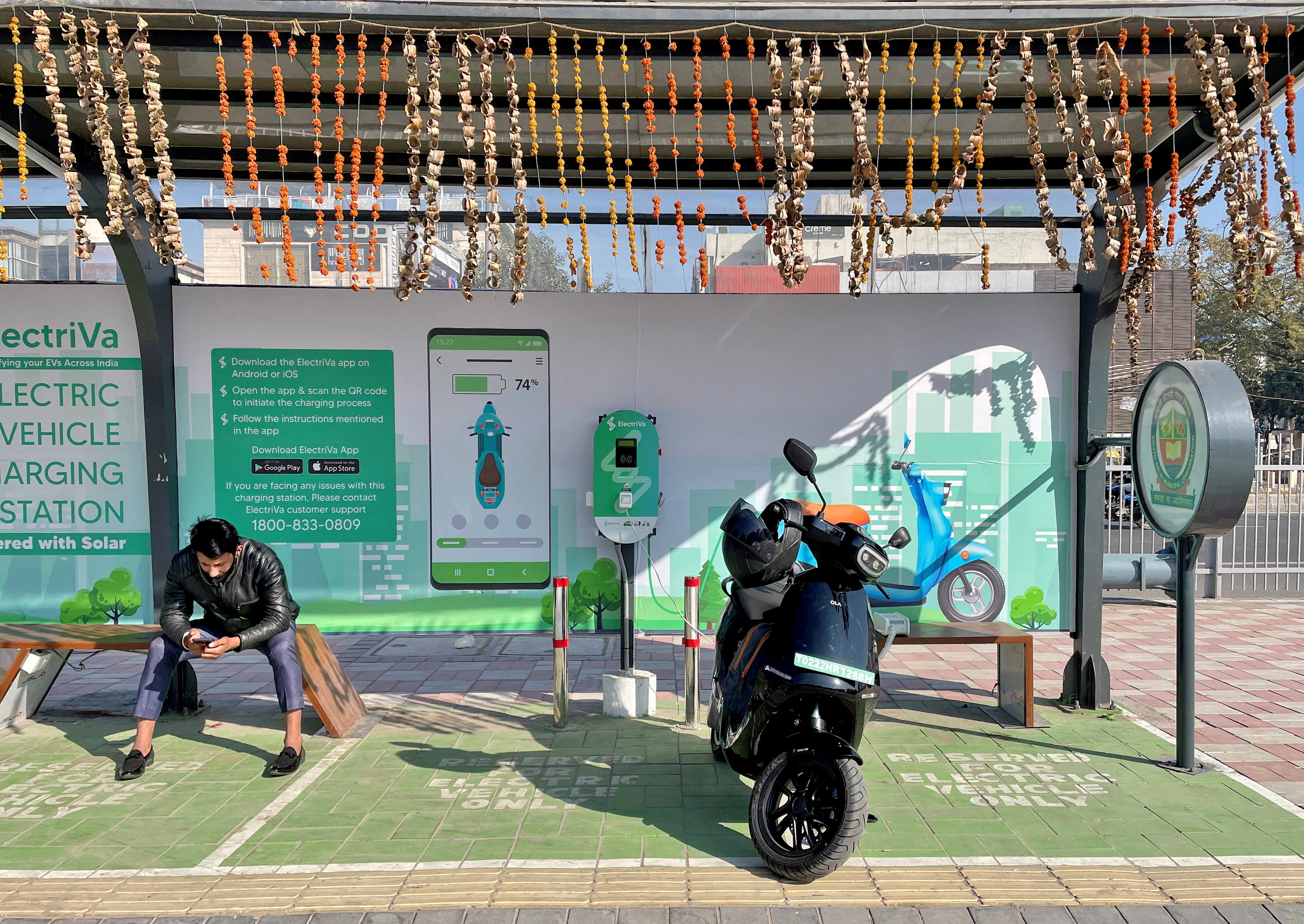 FILE PHOTO: A man checks his mobile phone as he waits while recharging his Ola electric scooter, in New Delhi