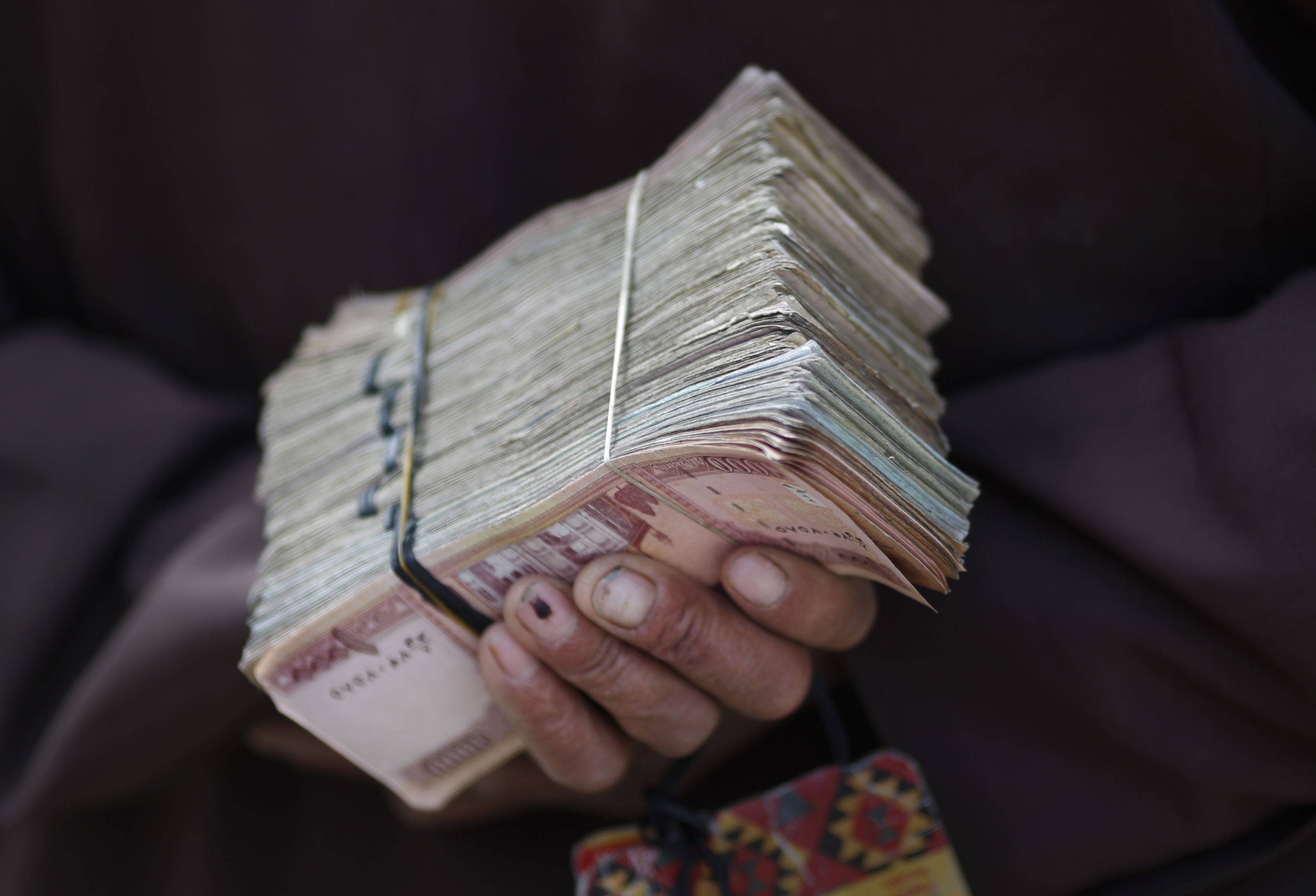 Money changer holds a stack of Afghan currency on a street in central Kabul