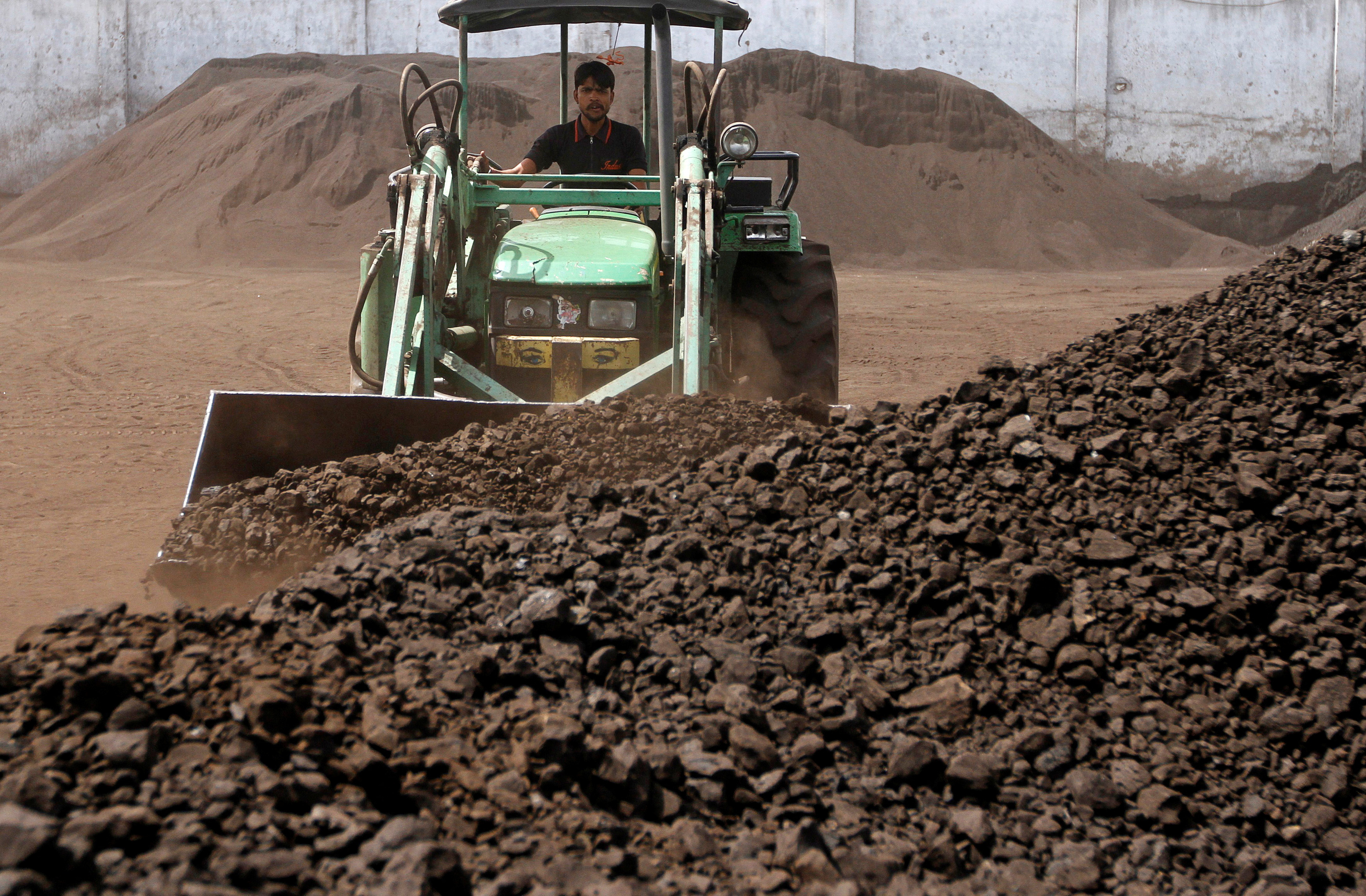 A worker uses a loader to assemble coal at a yard in the western Indian city of Ahmedabad