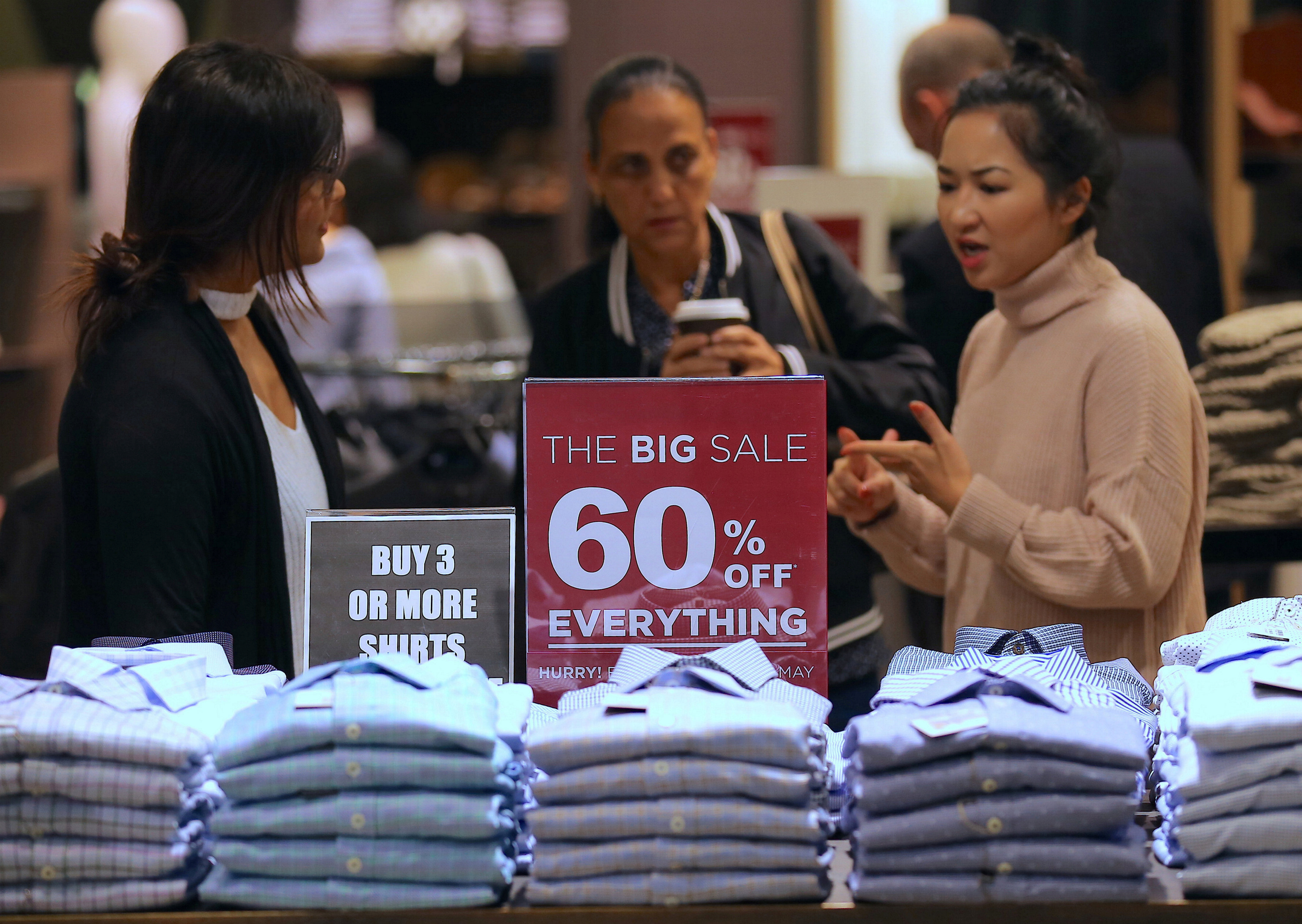 A shop assistant talks to customers in front of a sales sign on display at a retail store in central Sydney, Australia