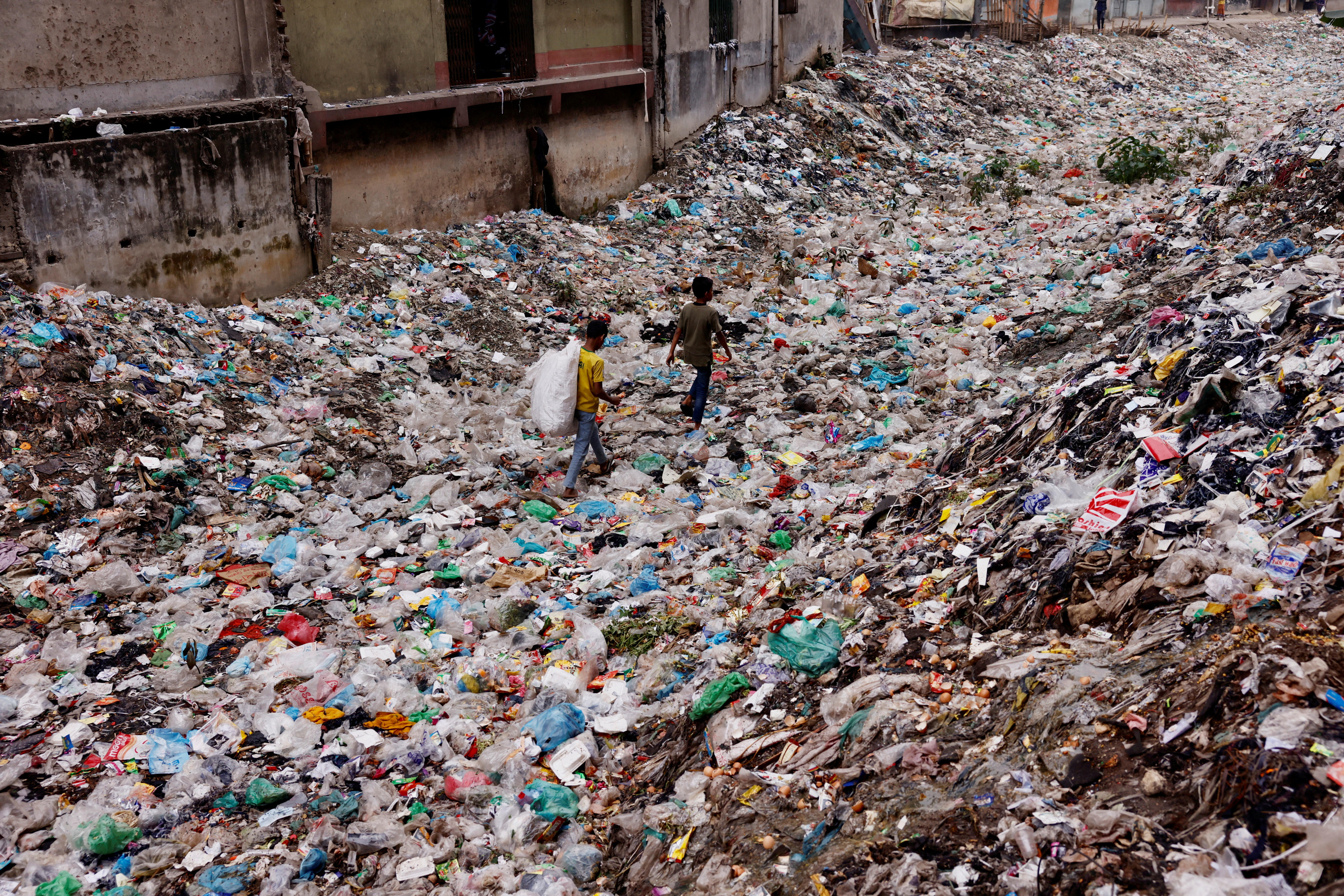 Children walk over a polluted area as they collect plastic materials in Dhaka