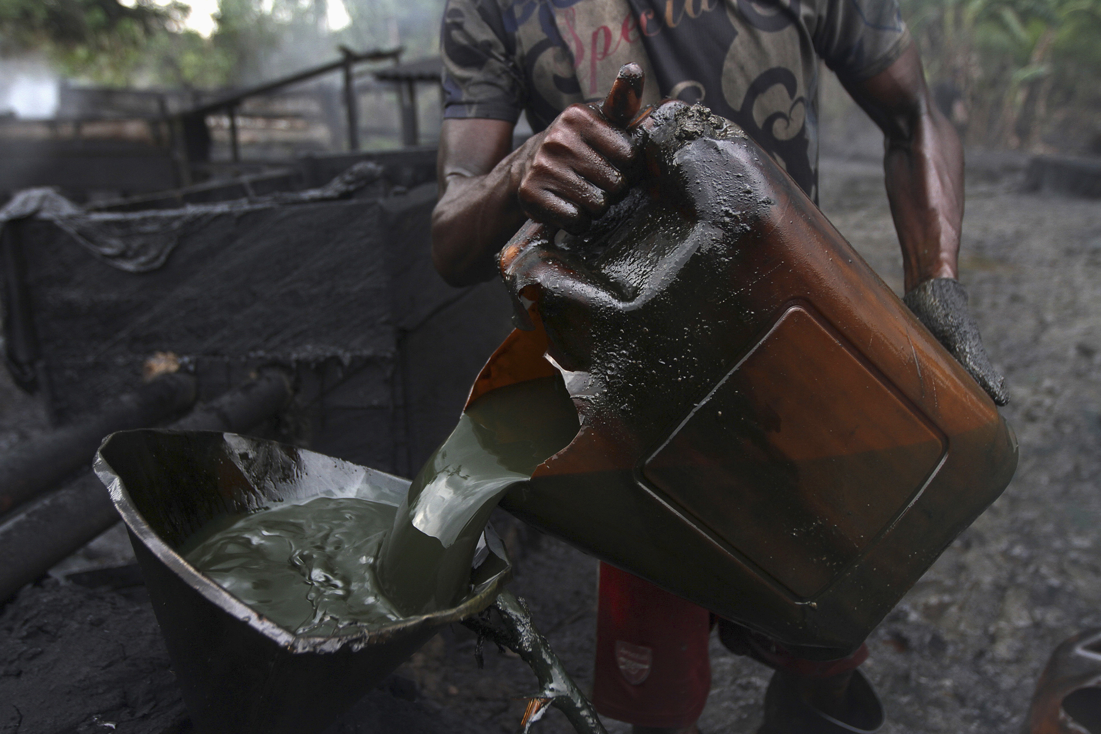 A worker pours crude oil into a locally made burner using a funnel at an illegal oil refinery site