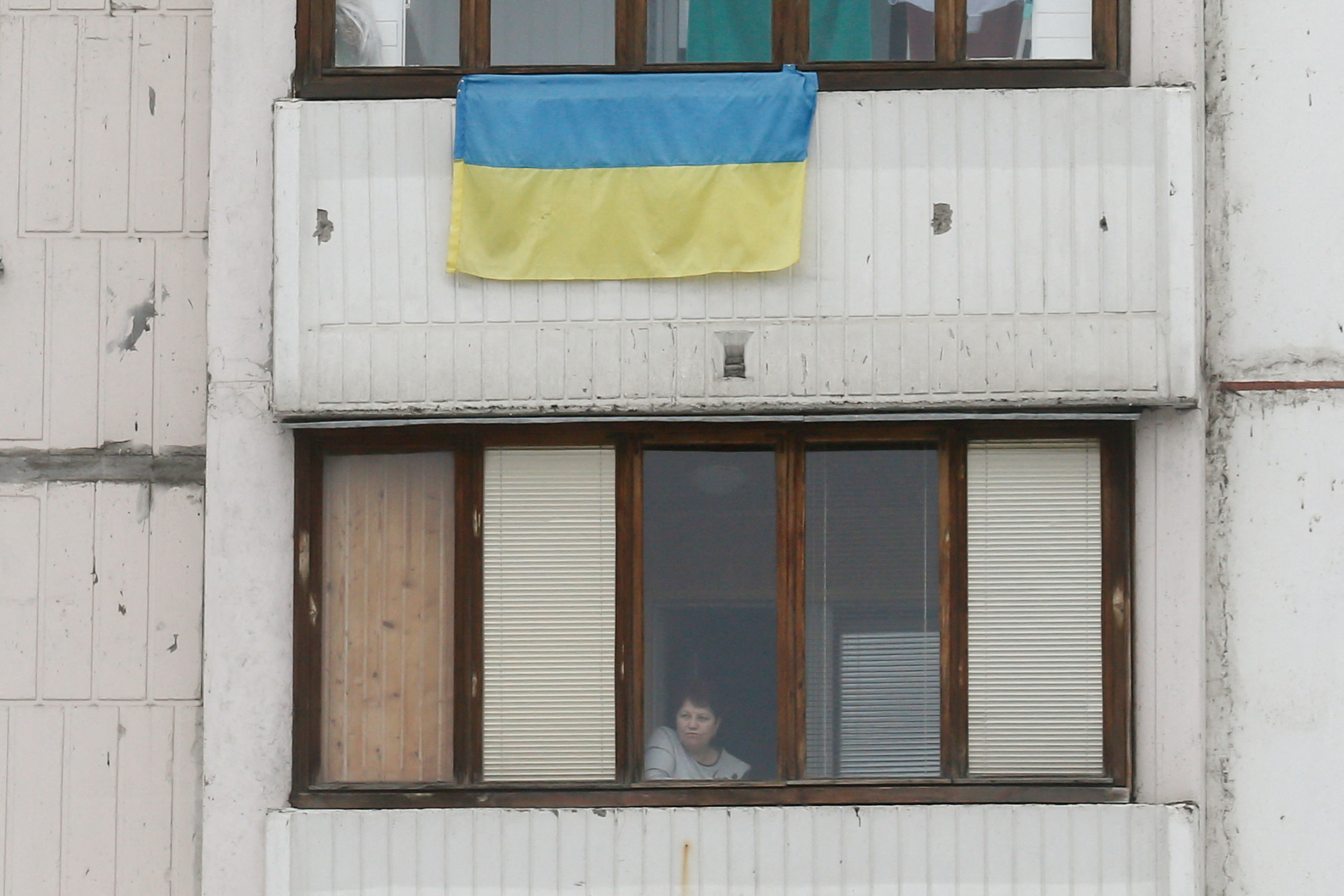 Woman looks out a window of her apartment, in Kyiv