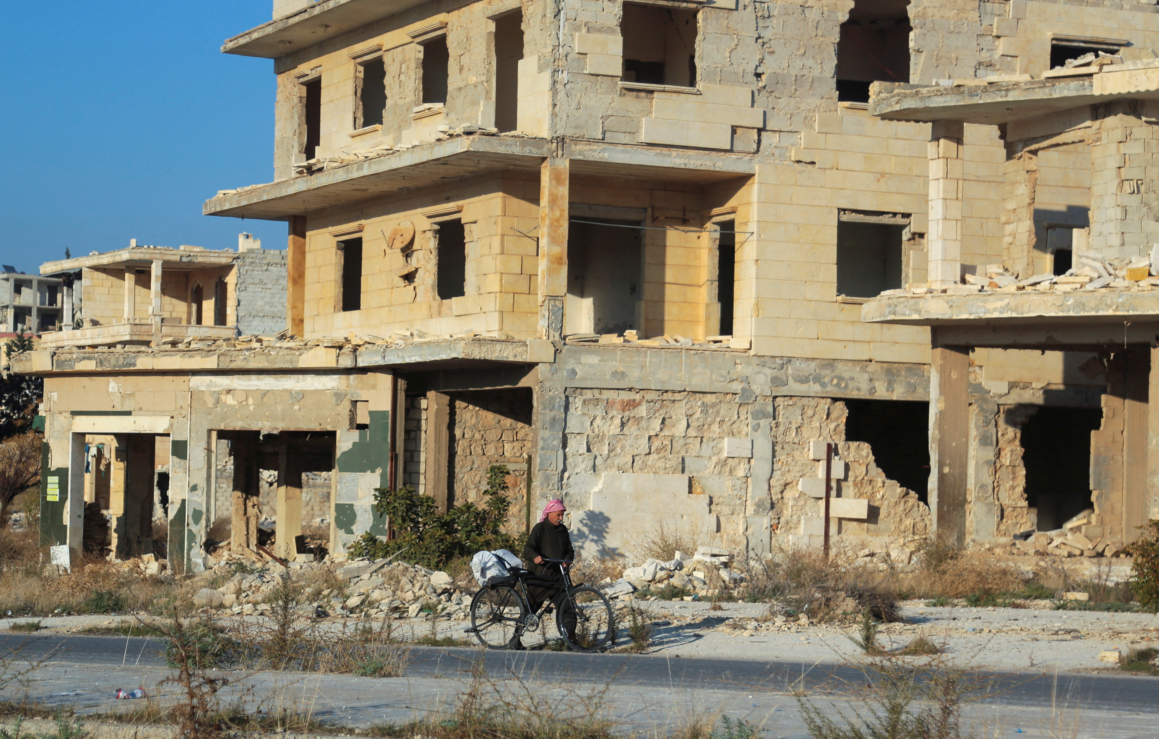 A man walks with his bike past damaged buildings in the town of Tel Rifaat