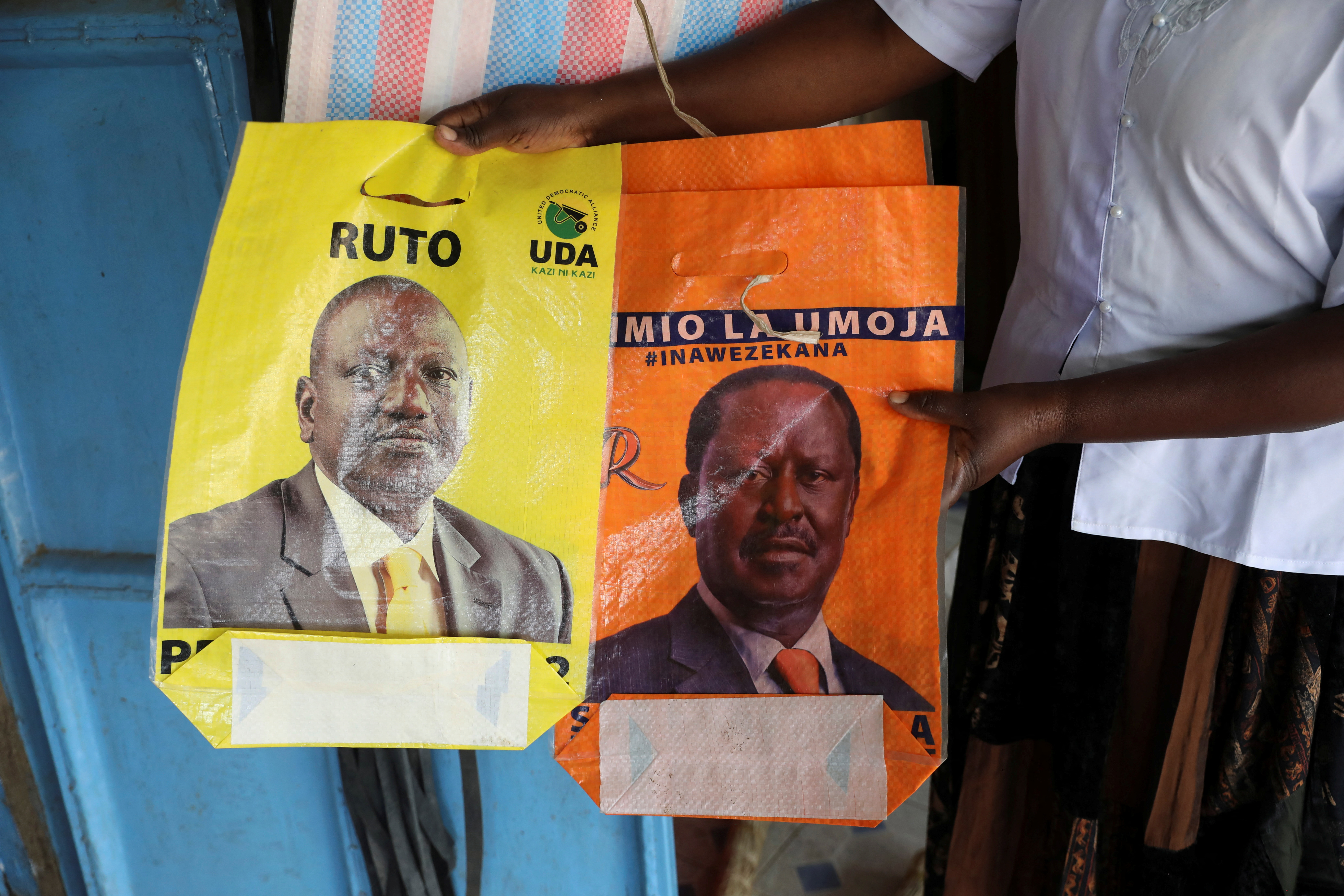 A shop owner hold bags depicting presidential candidate Raila Odinga and Deputy President William Ruto in the town of Kibigori