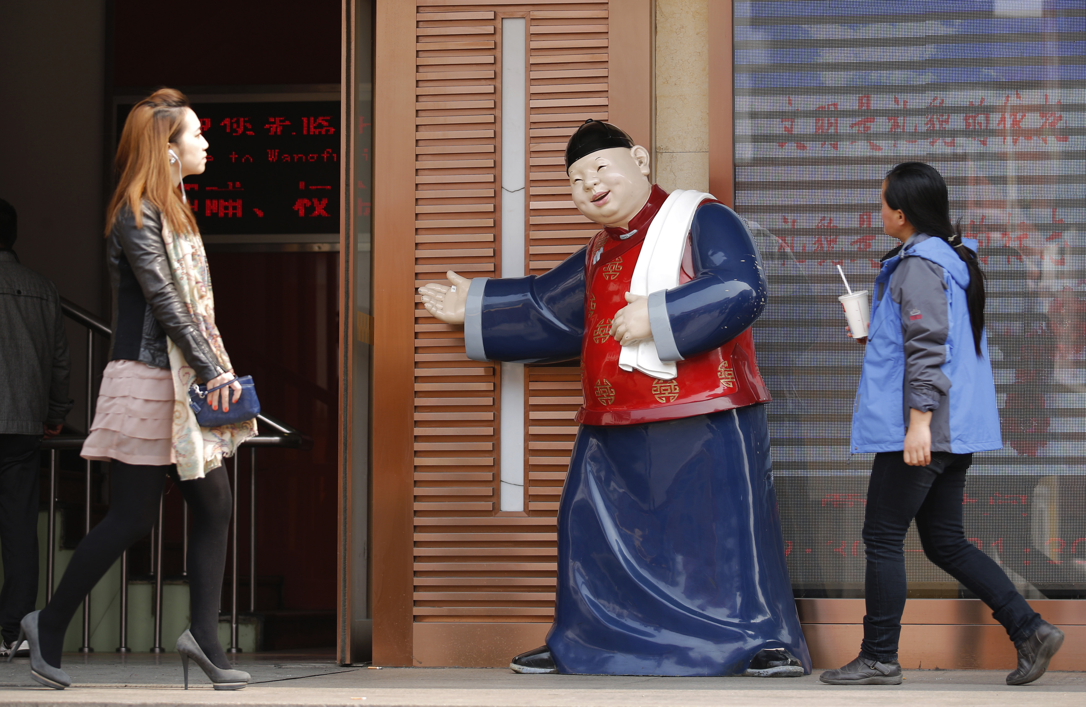 People walk past a statue, placed there to promote a restaurant, at a shopping district in Beijing