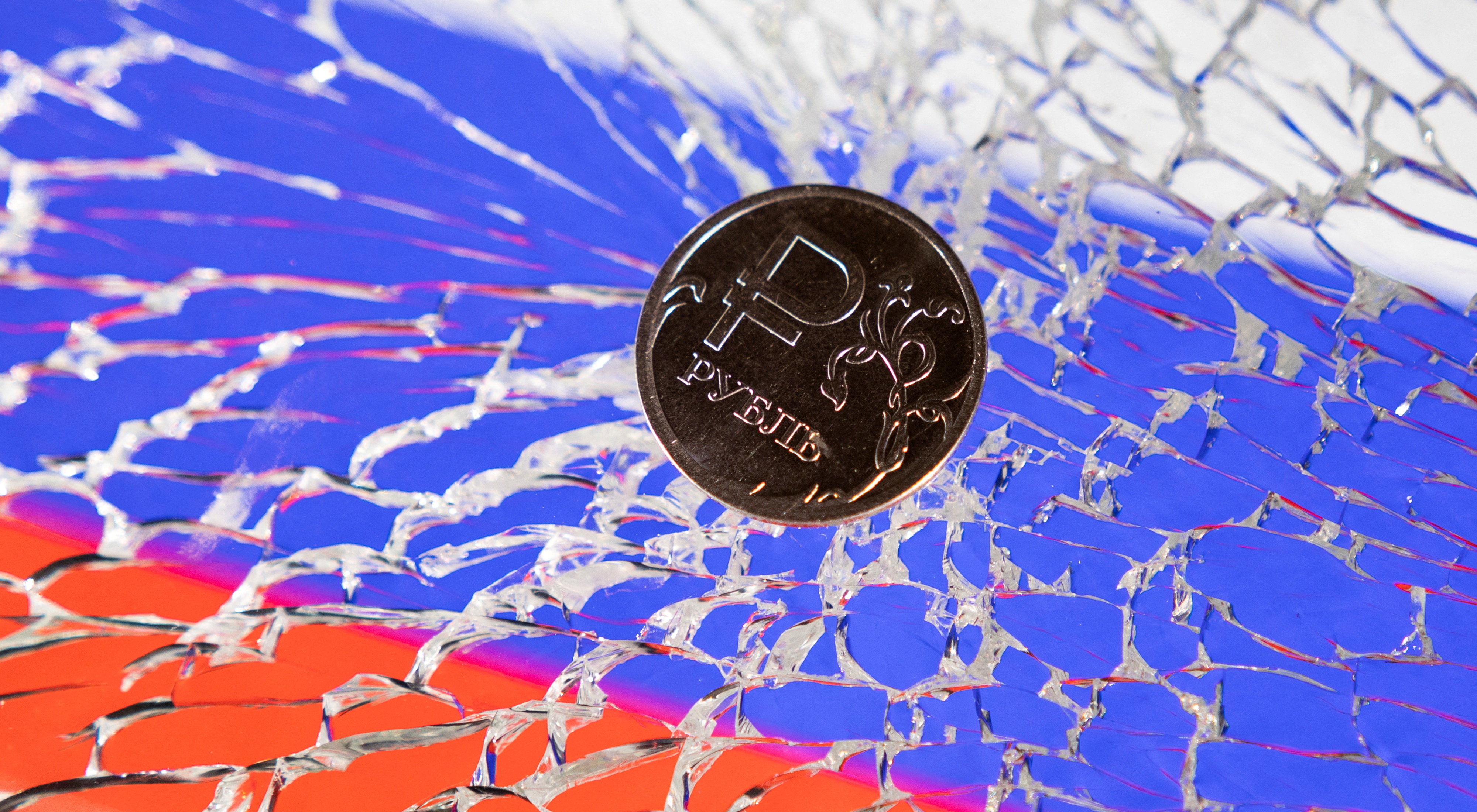 Illustration shows Russian Rouble coin is seen on a broken glass and displayed Russian's flag