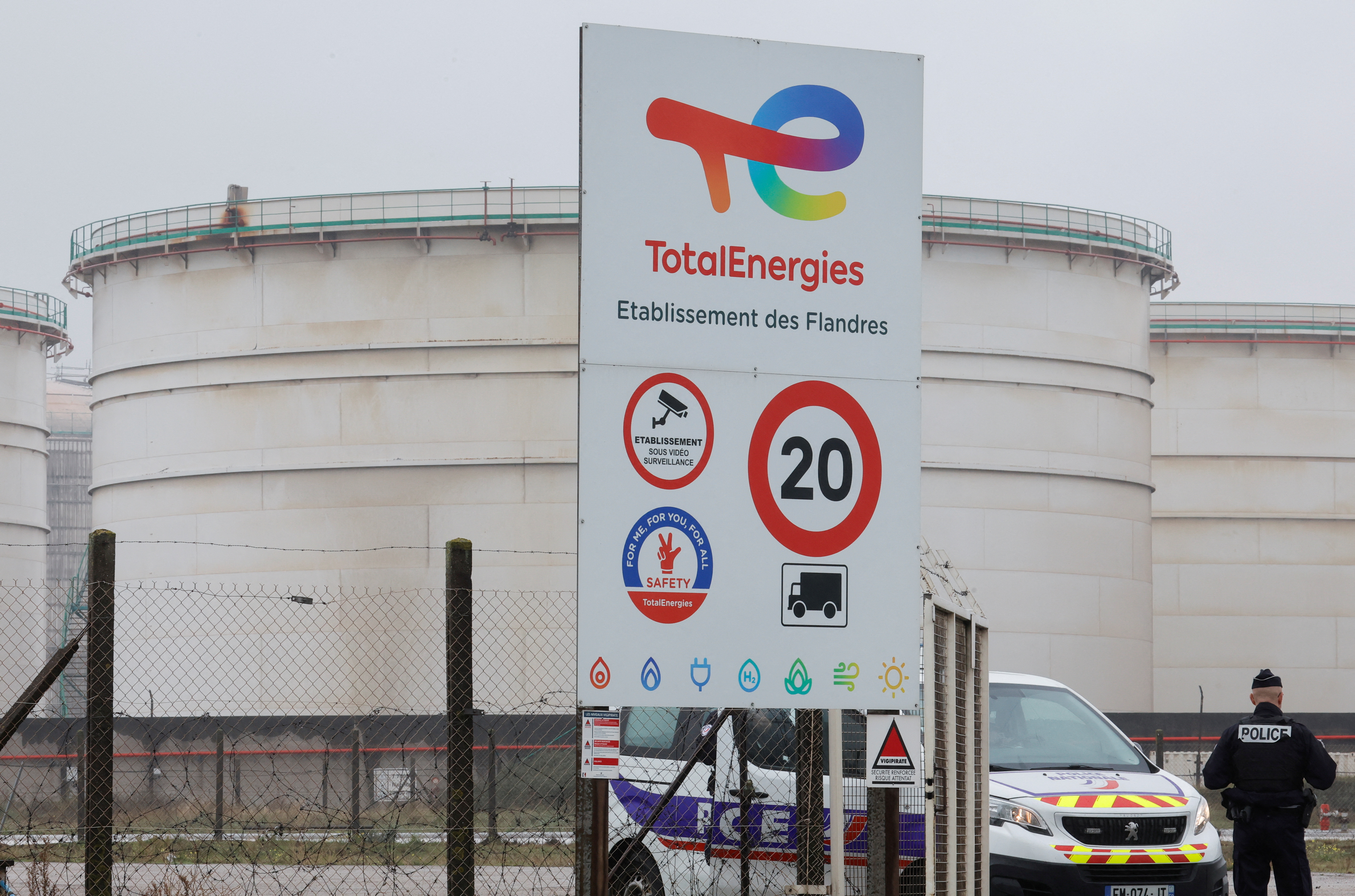 French policemen stand guard in front of giant TotalEnergies gasoline tanks of the former oil refinery in Mardyck