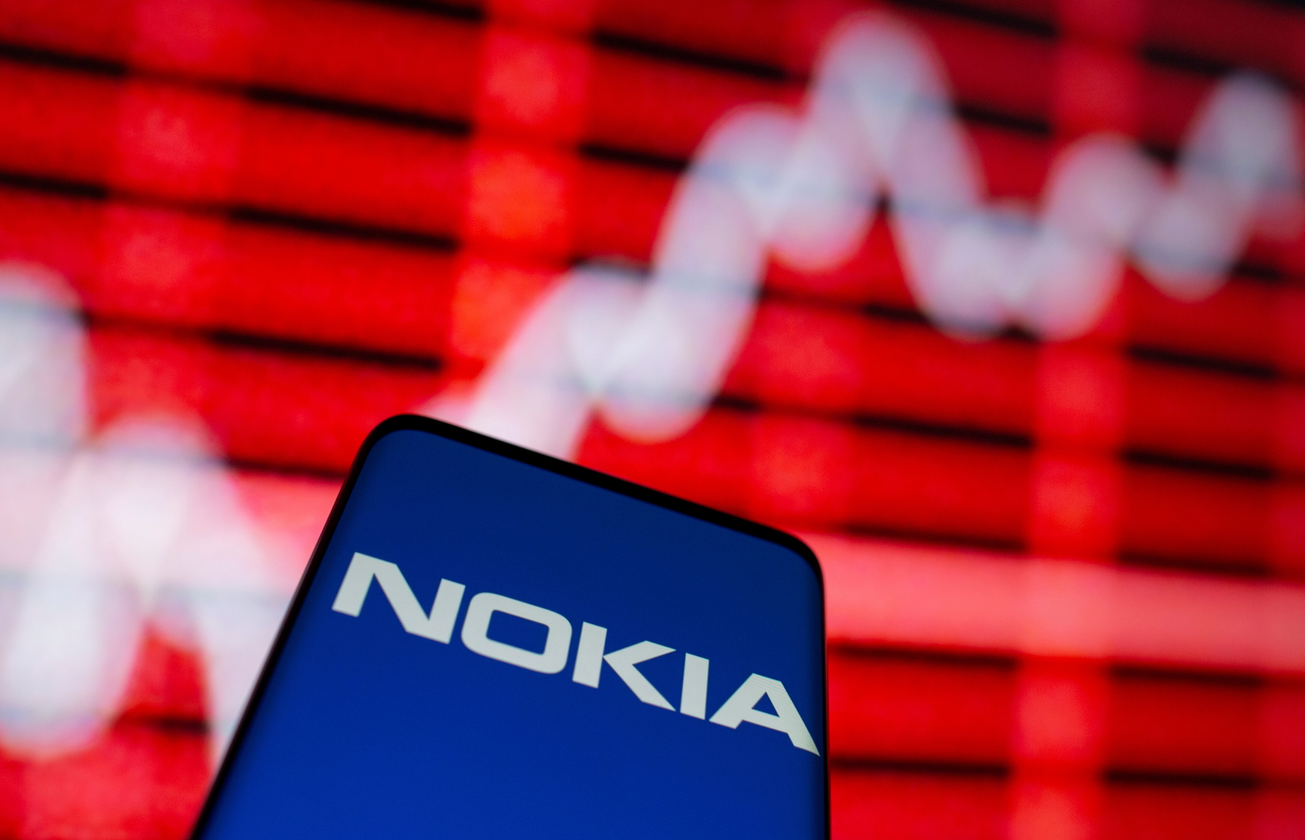 The Nokia logo is seen on a smartphone in front of a displayed stock graph in this illustration