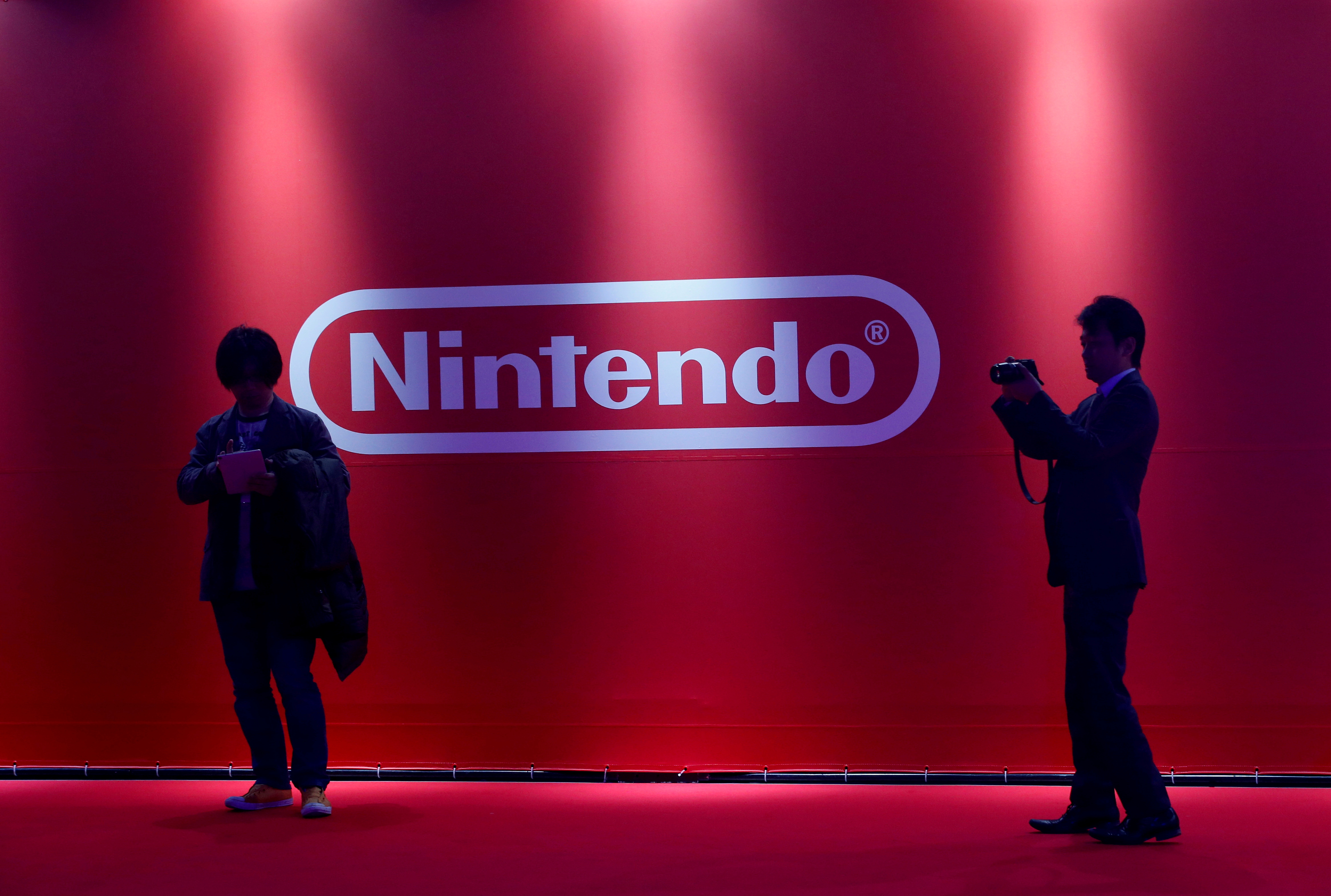 People stand in front of Nintendo's logo at the presentation ceremony of its new game console Switch in Tokyo