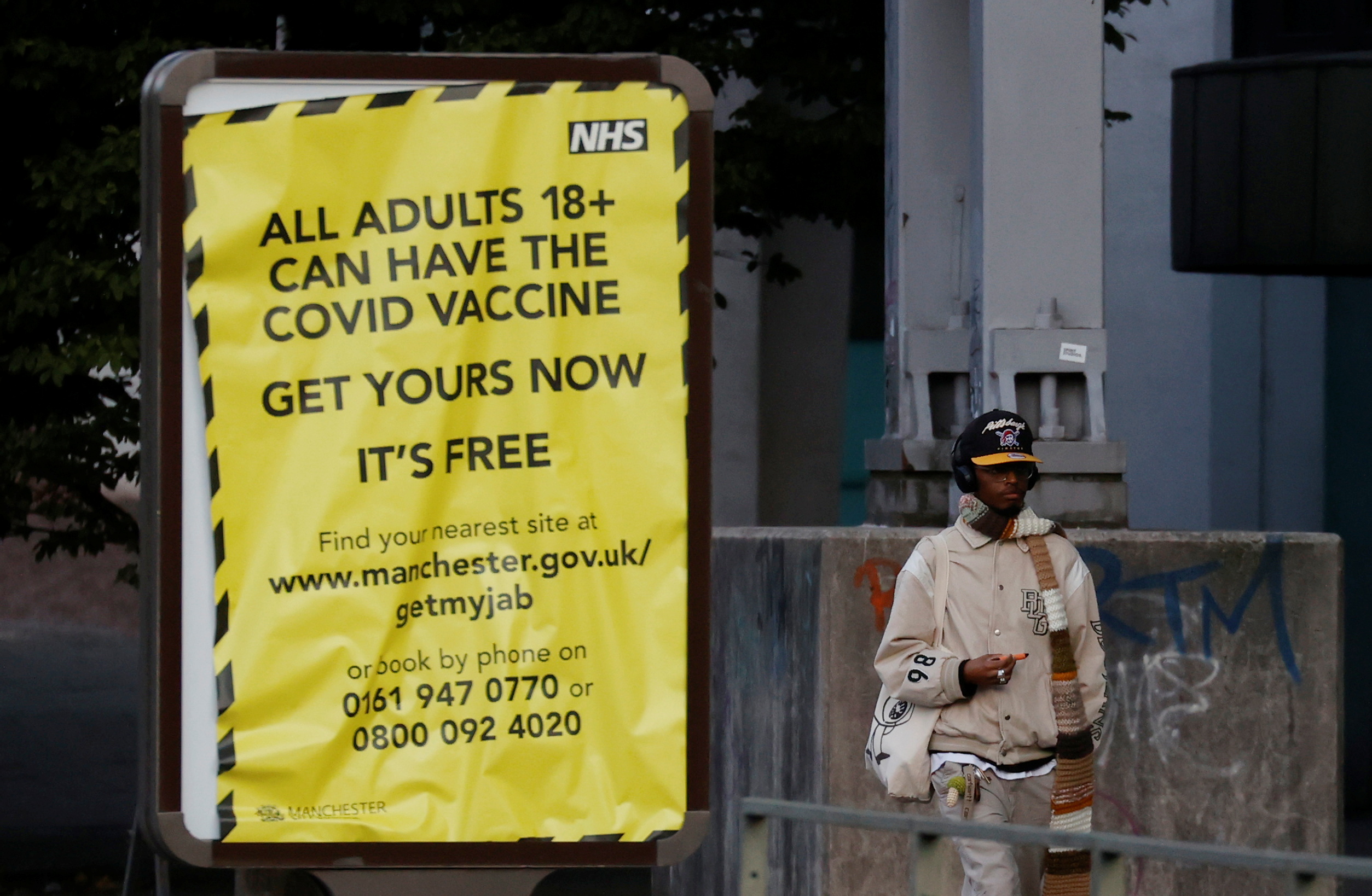 A man walks past a sign encouraging people to get their COVID-19 vaccine doses in Manchester