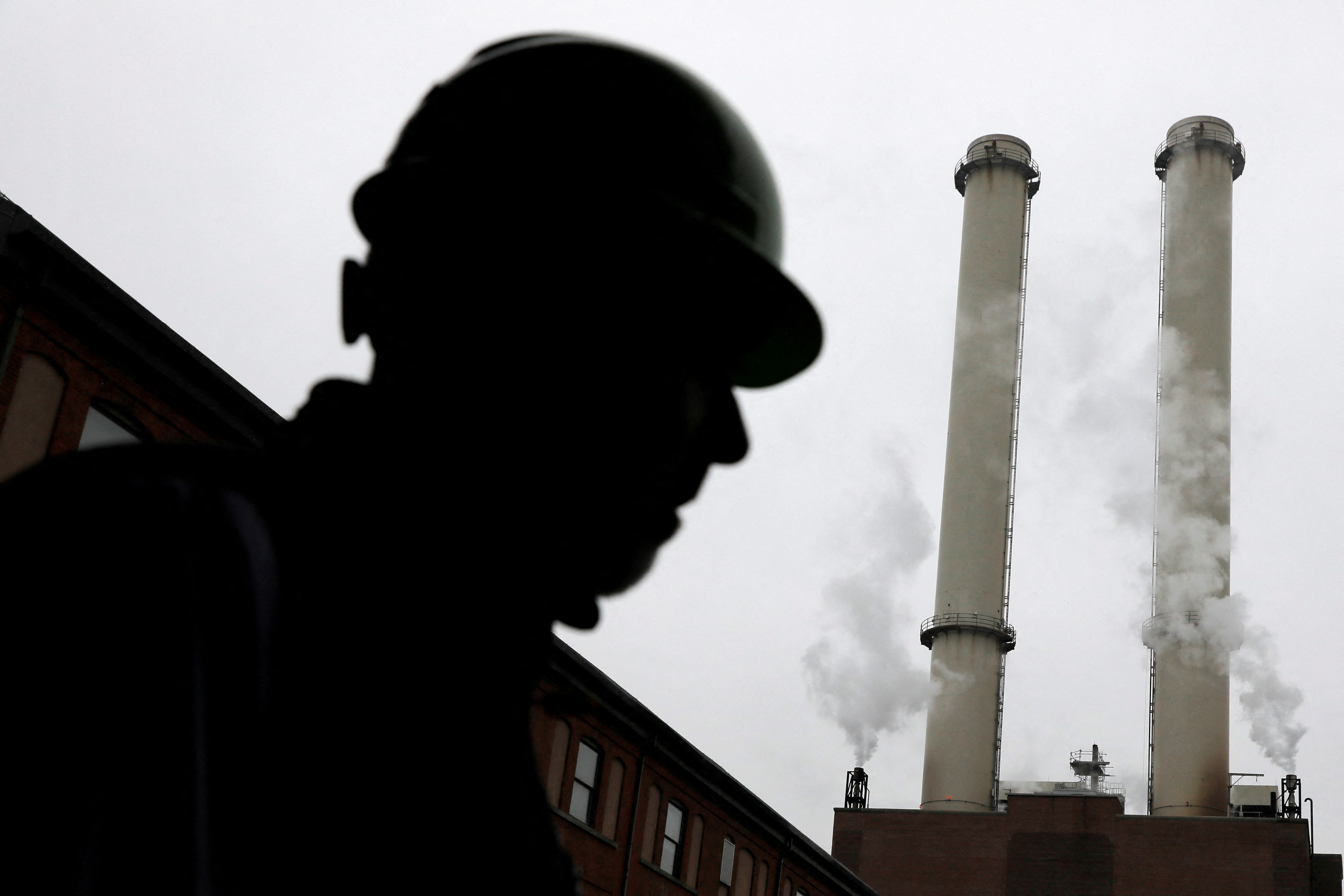 A worker stands near the chimney stacks of a neighbouring factory at IceStone, a manufacturer of recycled glass countertops and surfaces, in New York City