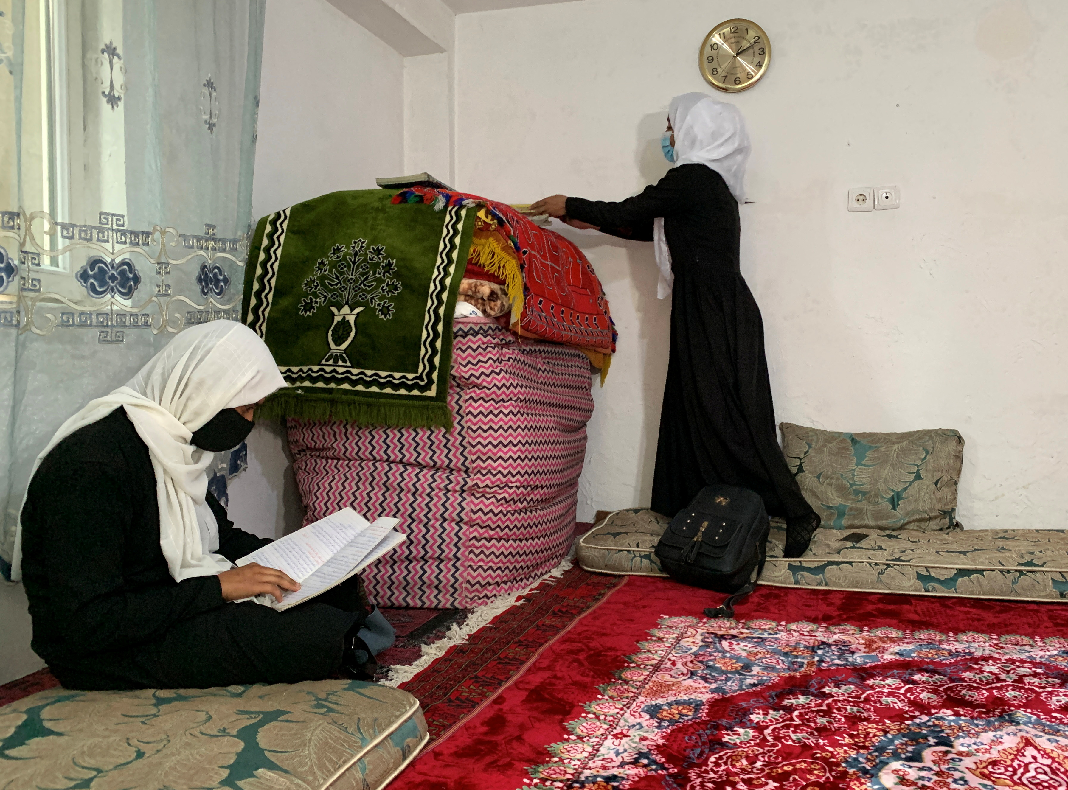 An Afghan schoolgirl reads from her notebook as another unpacks her school bag inside a house in Kabul