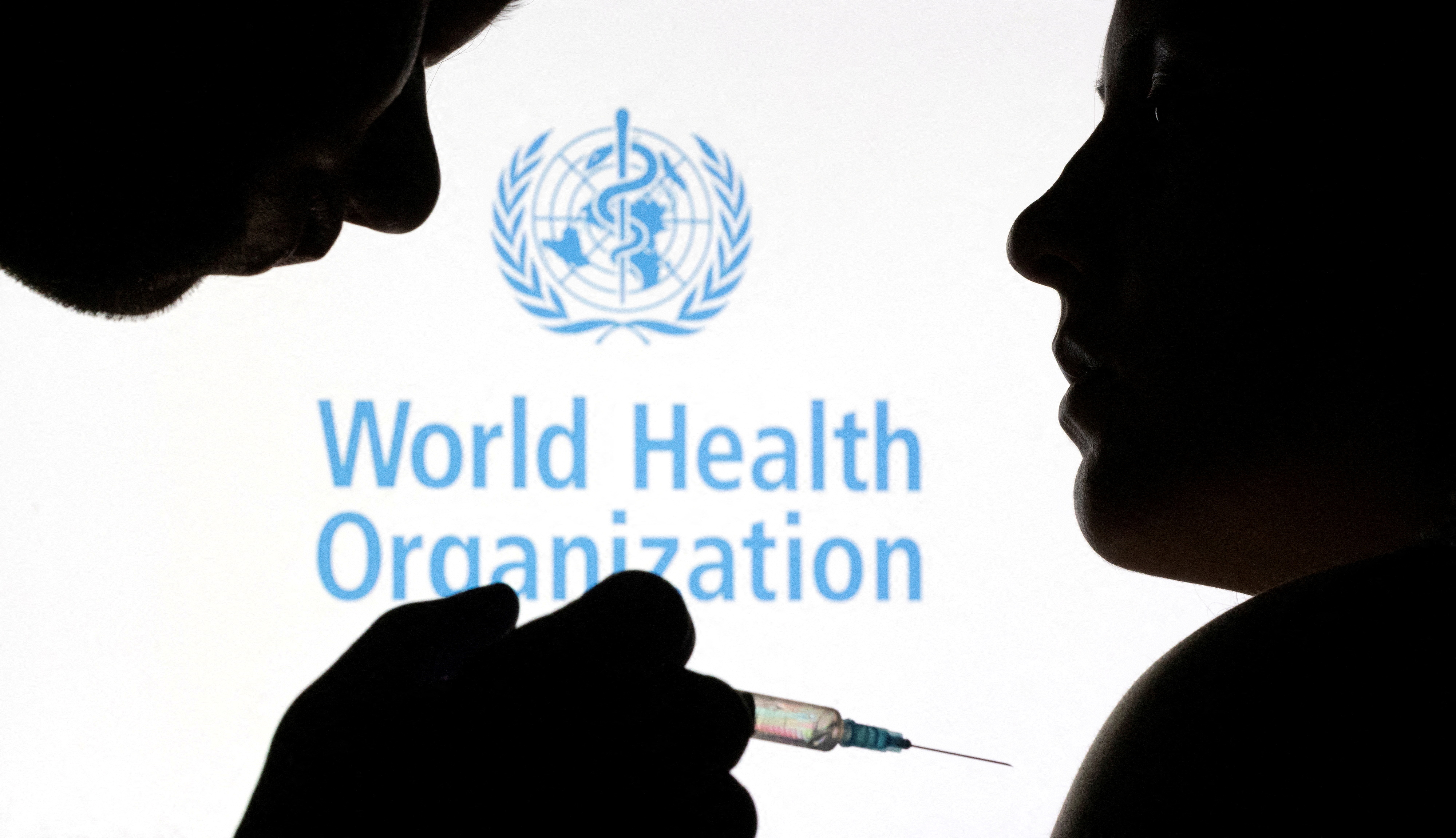 People pose with syringe and needle in front of displayed WHO logo