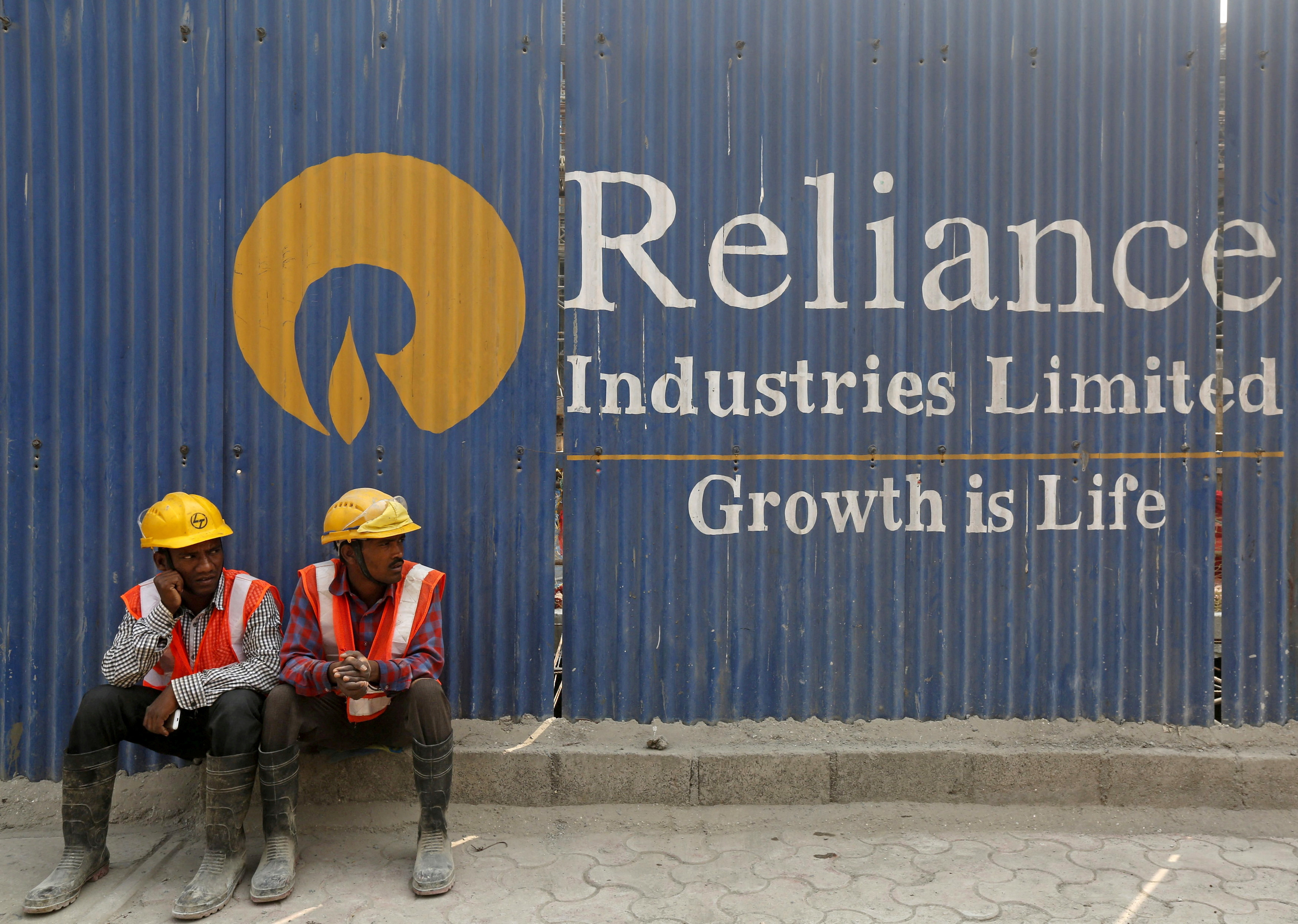 Labourers rest in front of an advertisement of Reliance Industries Limited at a construction site in Mumbai