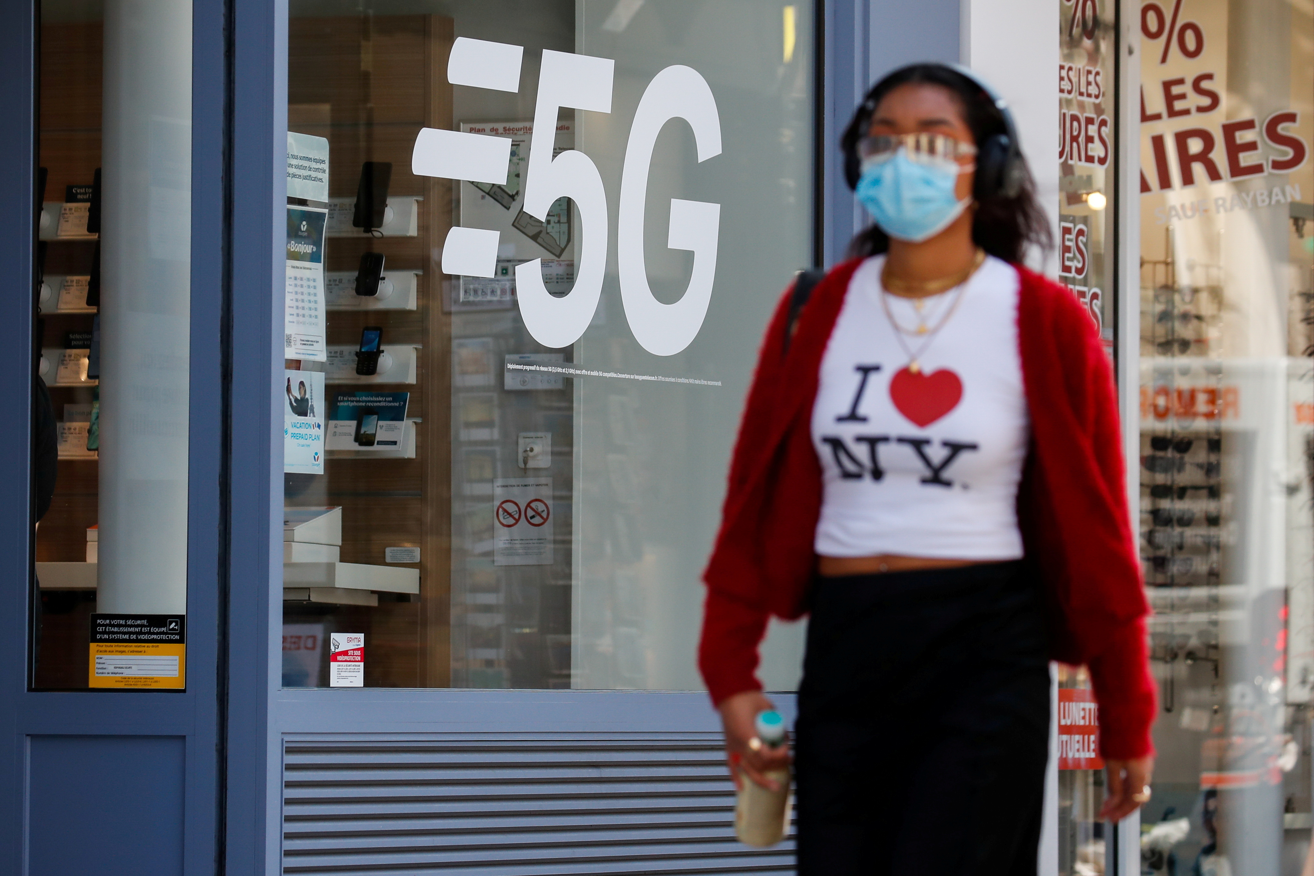 A woman, wearing a protective face mask, walks past a 5G data network sign at a mobile phone store in Paris, France, April 22, 2021. REUTERS/Gonzalo Fuentes