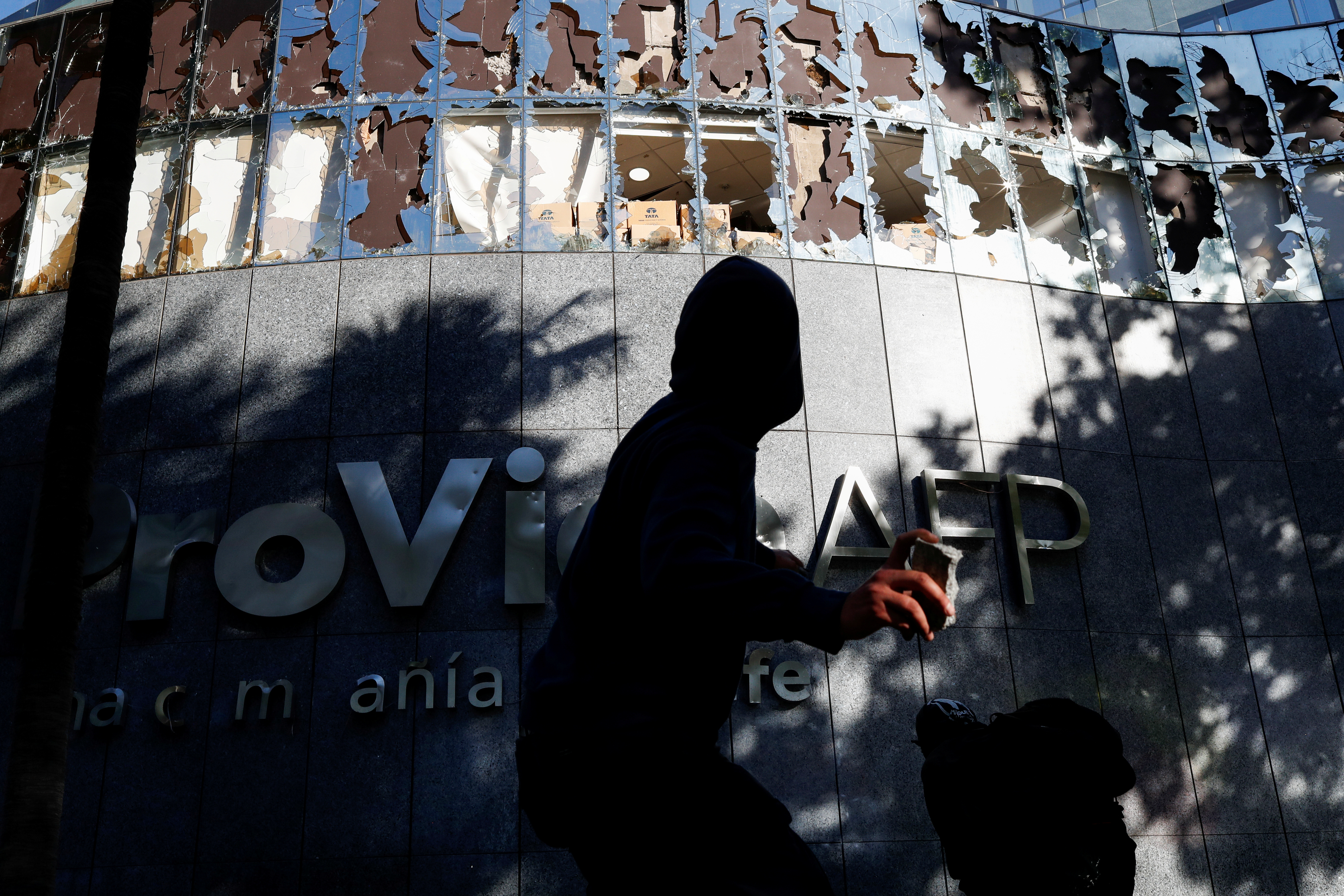 A demonstrator throws a stone to a Chilean Pension Fund Administrator (AFP) building during a protest at Providencia, a wealthy neighborhood, in Santiago