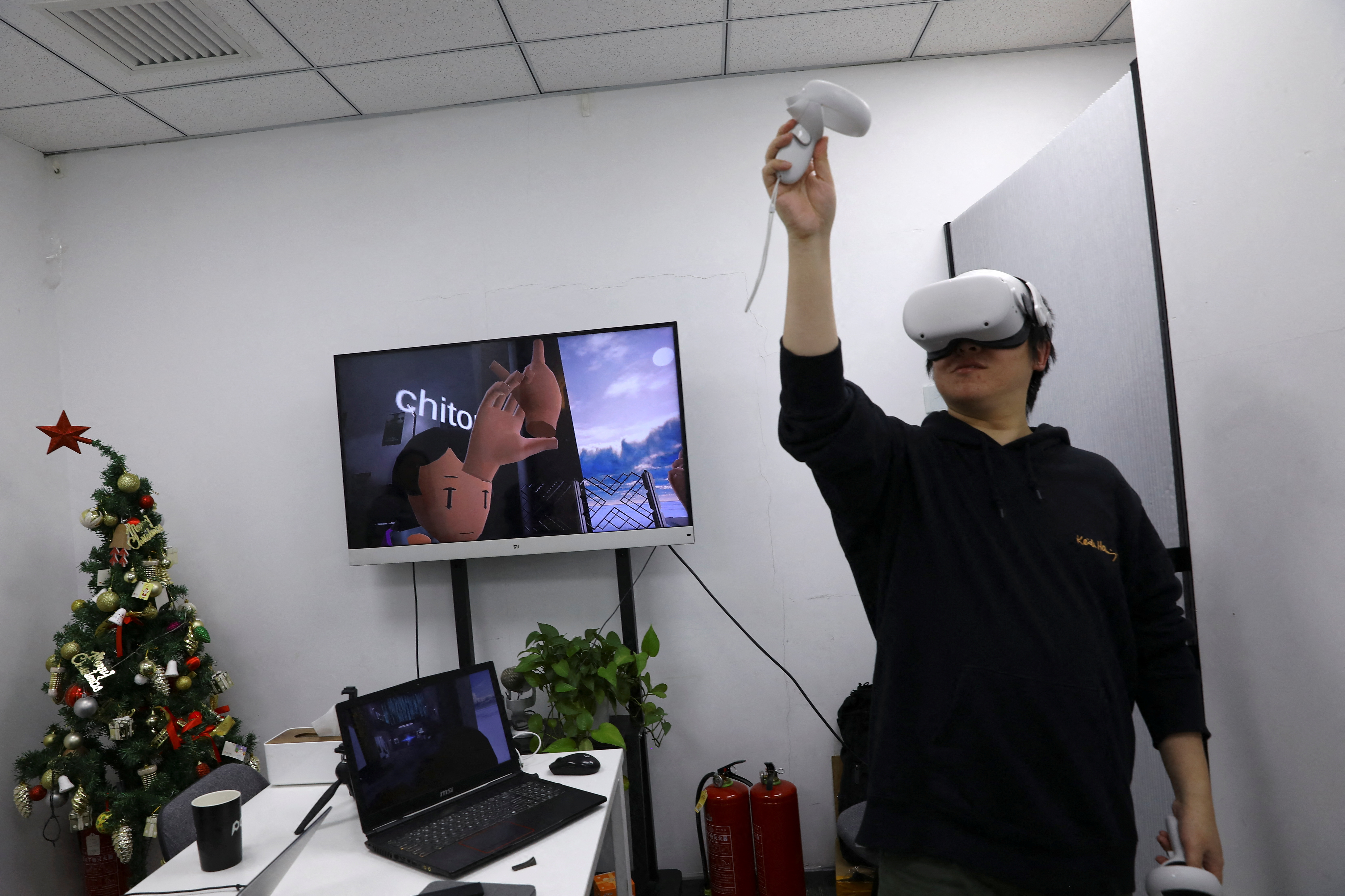 Pan Bohang, founder of vHome, a VR social gaming platform, wearing VR goggles greets with a user during a virtual gathering, at an office in Beijing