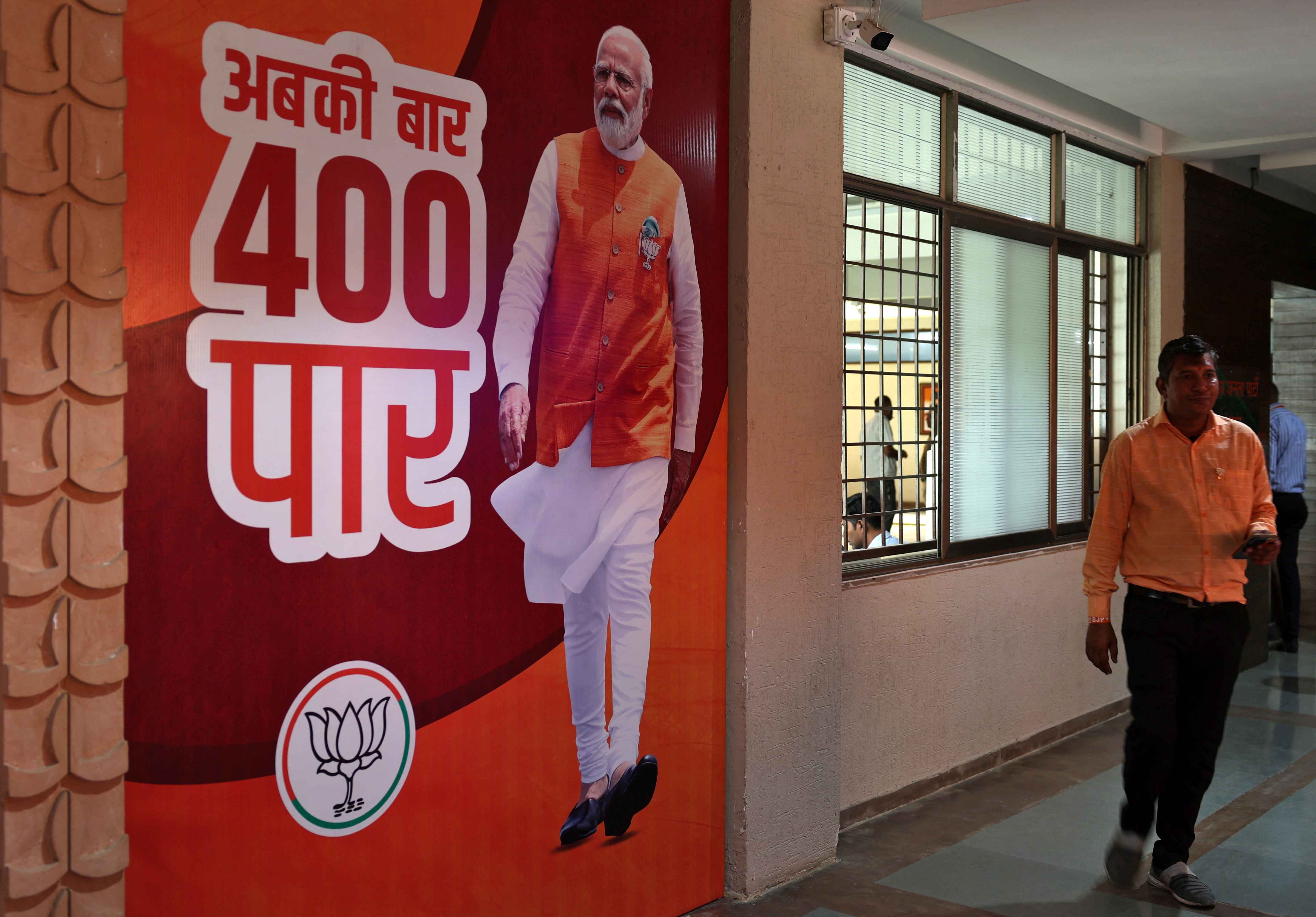 Supporter of Bharatiya Janata Party walks past a poster of Prime Minister Narendra Modi at its party's state headquarter in Gandhinagar