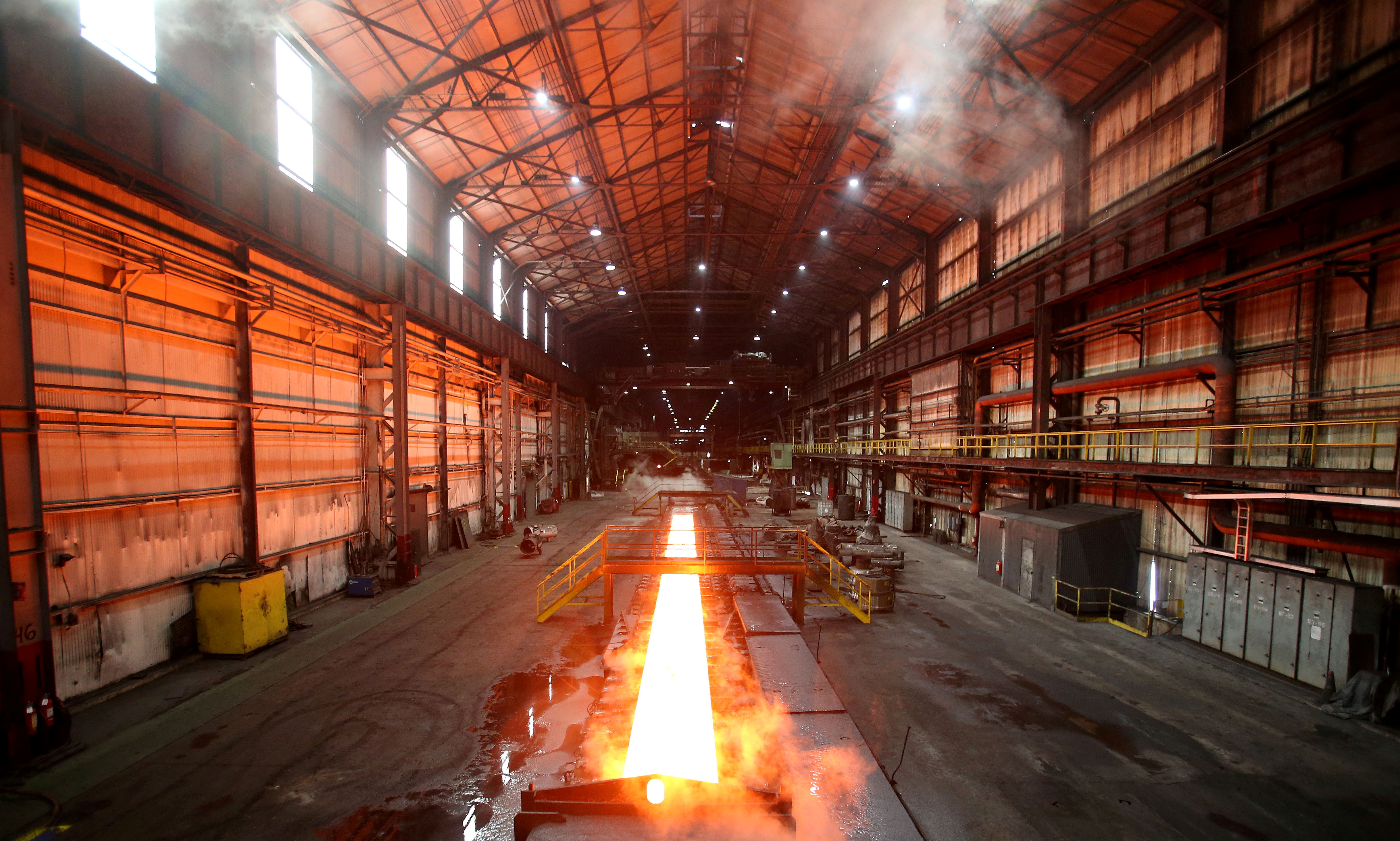 Steam rolls off a slab of steel as it rolls down the line at the Novolipetsk Steel PAO steel mill in Farrell