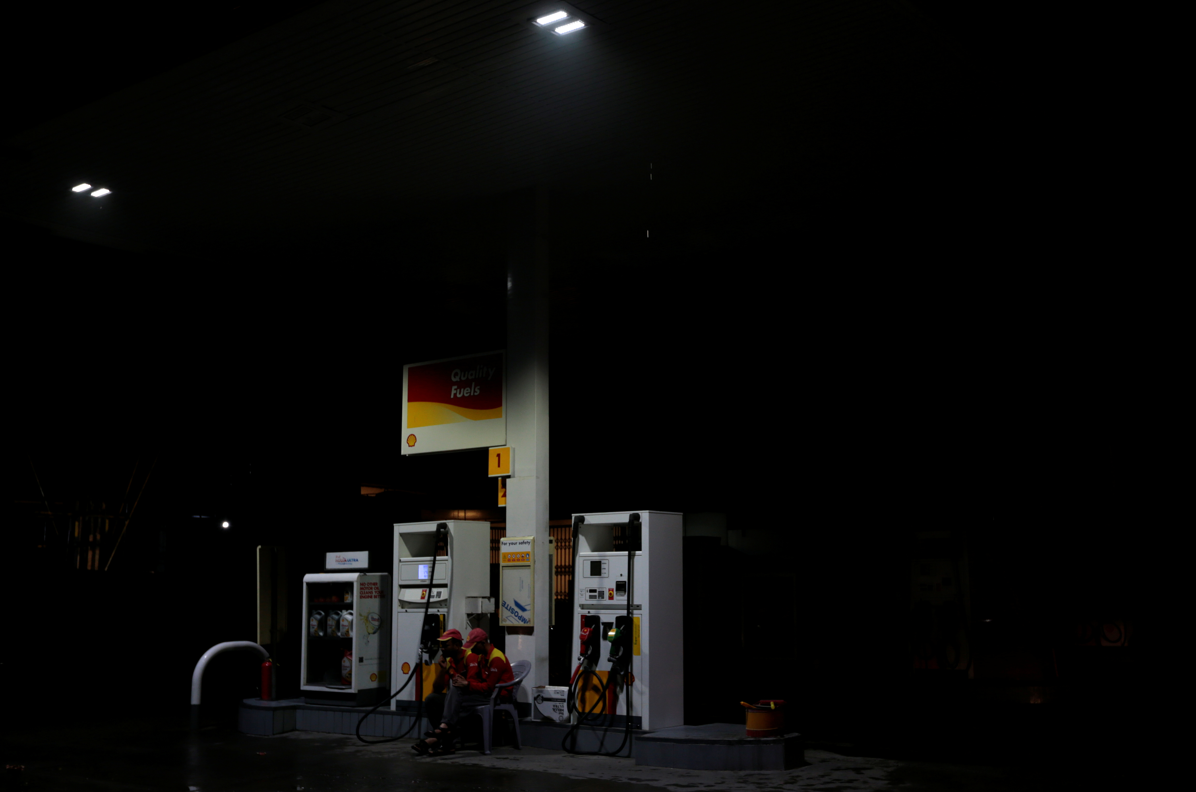 Employees sit next to fuel pumps as they close the petrol station after running out of petrol, in Islamabad
